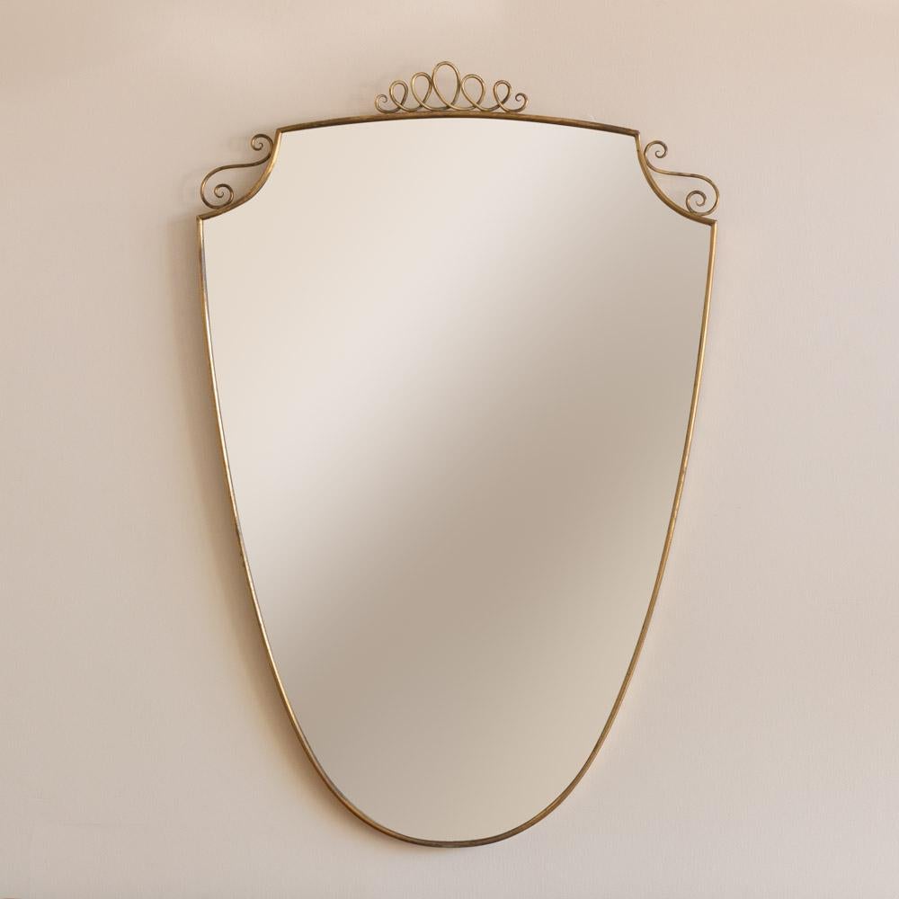 Grand miroir italien en laiton en forme de bouclier avec détail de boucle en laiton sur le dessus, années 1950. Finition originale en laiton avec une belle patine d'âge. 