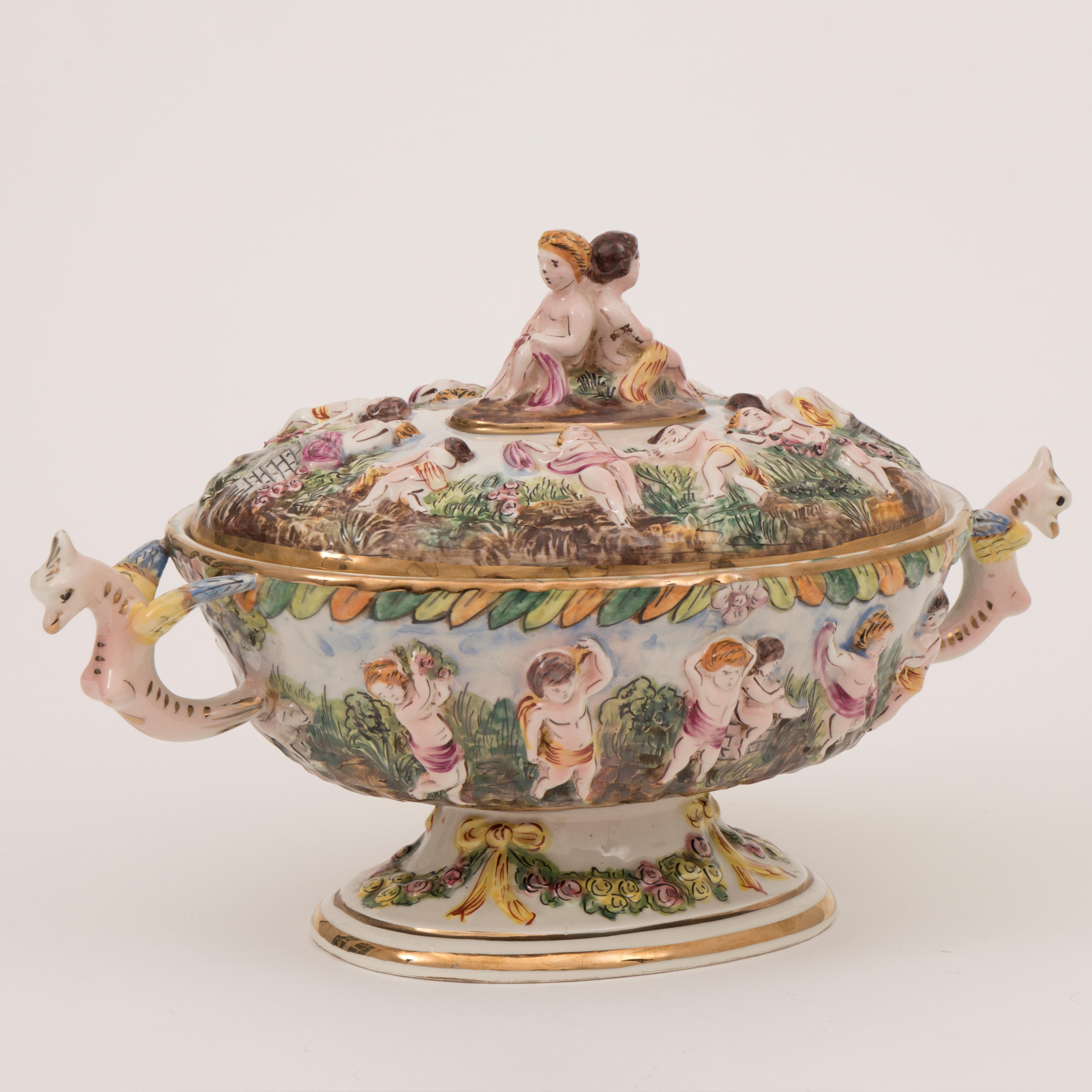 1950s vintage large Italian Capodimonte porcelain serving tureen decorated on the lid and around the outside with an array of dancing cherubs in a mythological garden. Winged breasted fawns form the matching handles on either side to help which help