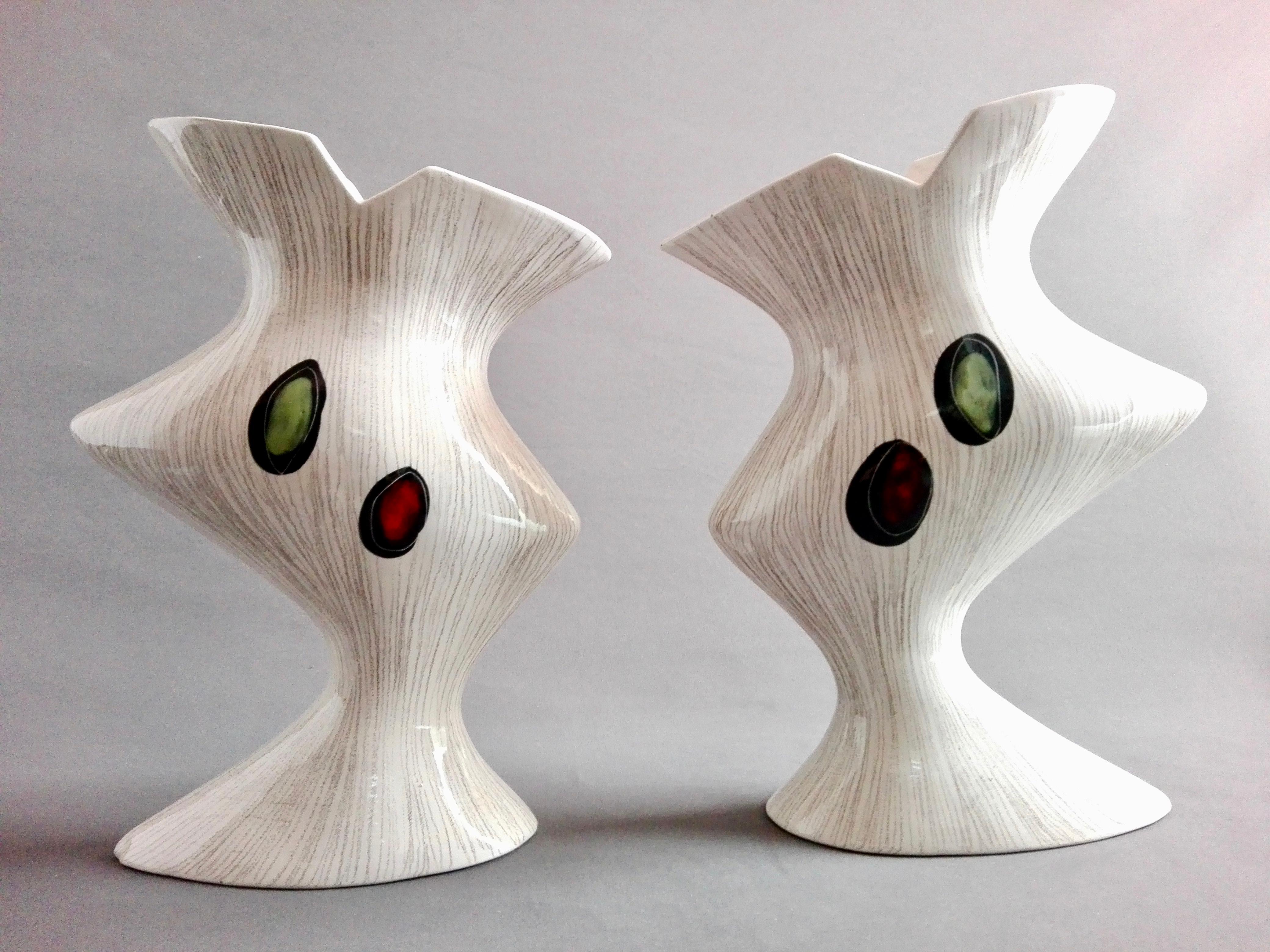 Elegant pair of asymmetrical multicolored decorated white Italian ceramic vases from the late 1950s-early 1960s. They have a mirrored shape with decorative double-sided hand-made subjects.
The decoration was done using glazed colours and sgraffito