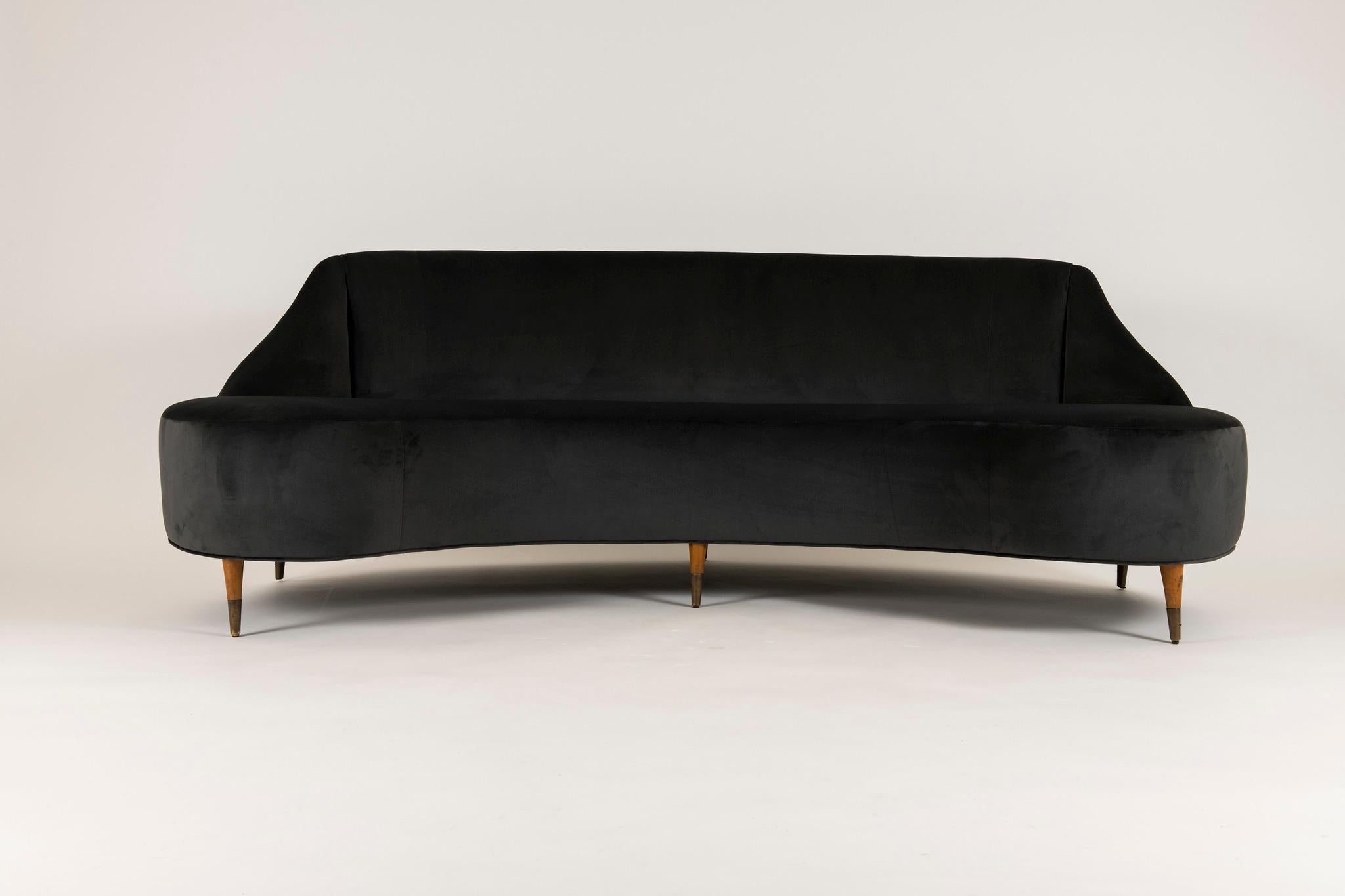 A low lying 1950s Italian curved back sofa with wooden legs and brass sabots, professionally upholstered in a contemporary charcoal velvet. 

Inside Seat Depth: 18.75