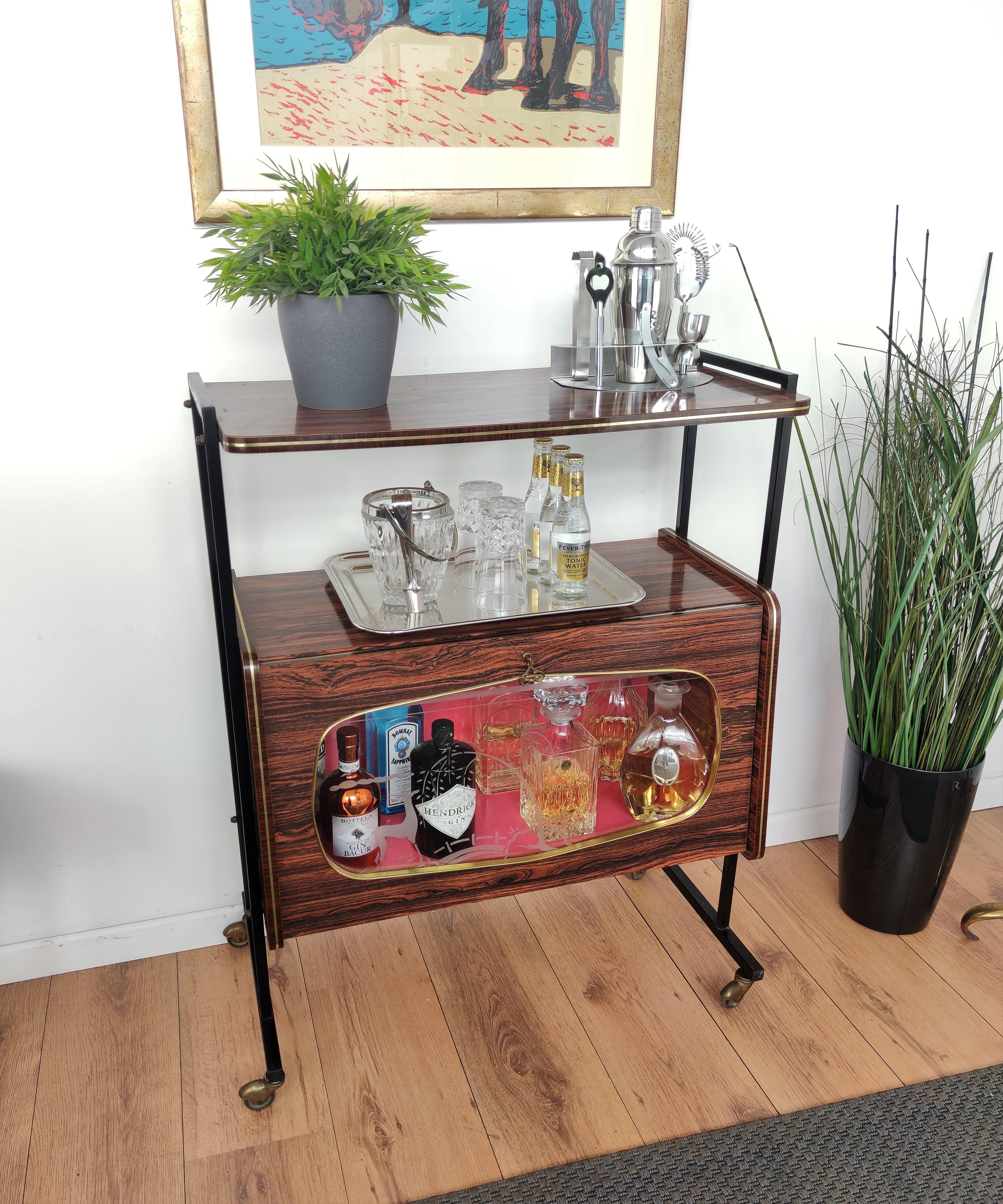 Very elegant Italian midcentury two-tier greatly shaped dry bar cabinet cart, in walnut wood and brass line details. The beautiful front flip brass and decorated glass door allow to see the amazing interior part lined in pinkish color, all standing
