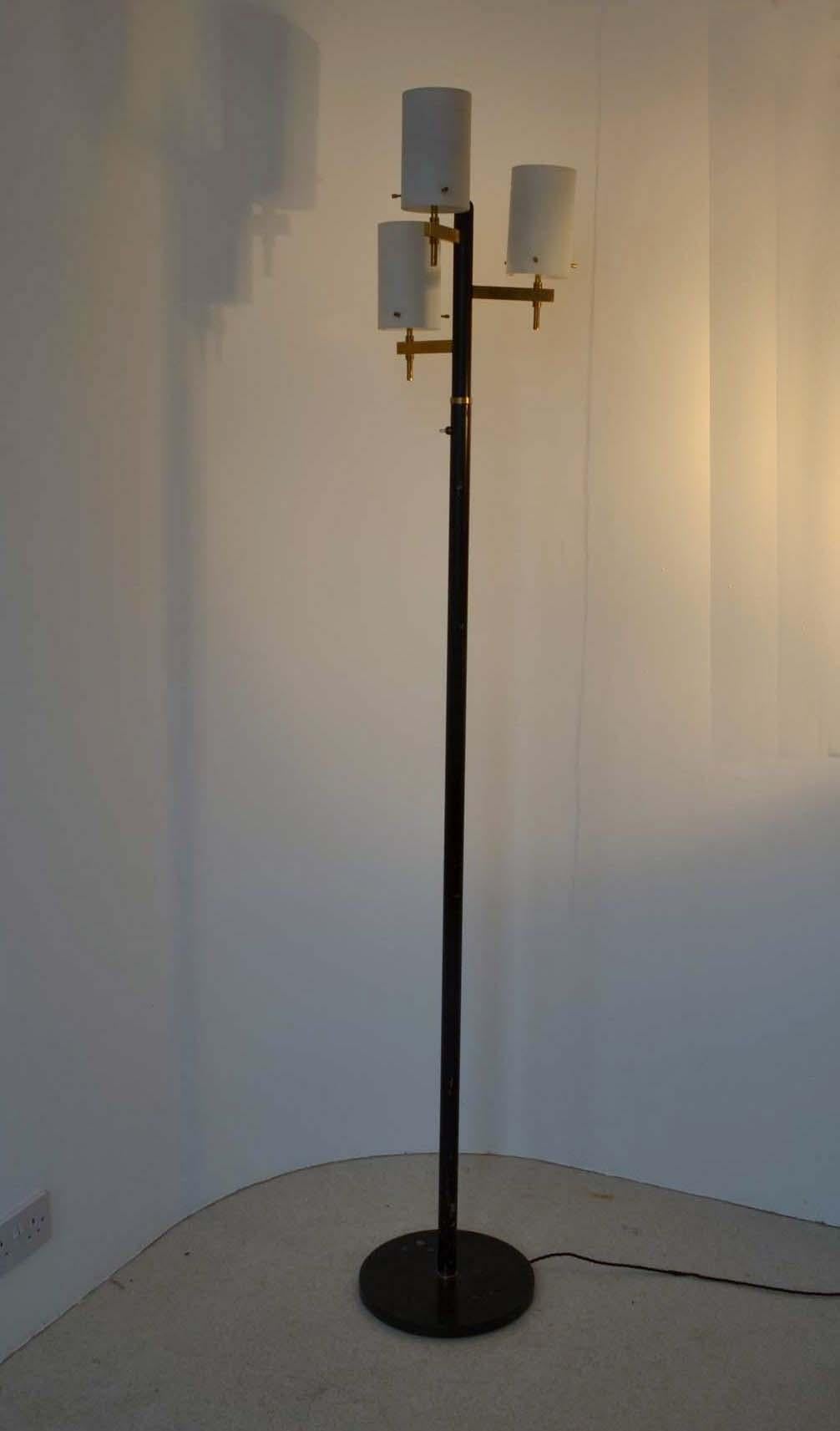 The Italian 1950s floor lamp is attributed to Stilnovo having all the elements associated with the company combining glass, enameled black steel, brass and marble. The three brass arms each hold opaline white cylindrical shades, centered by tall