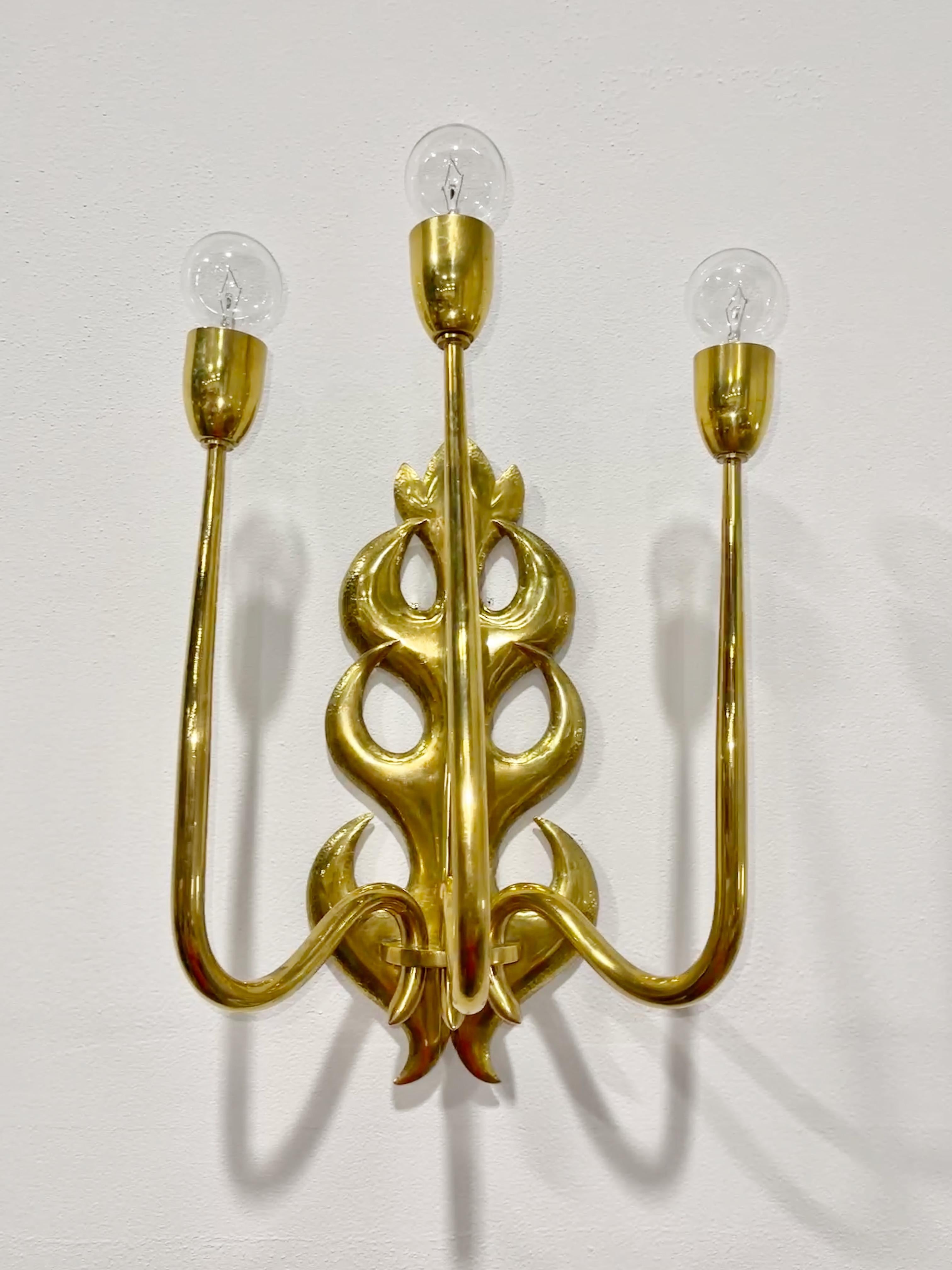 A single grand scale 1950s Italian brass three arm wall lamp in the manner of Osvaldo Borsani and Tomaso Buzzi.
Backplate is hand hammered and chased brass in the form of modernistic acanthus leaves.
Three curvaceous tapered brass arms topped with