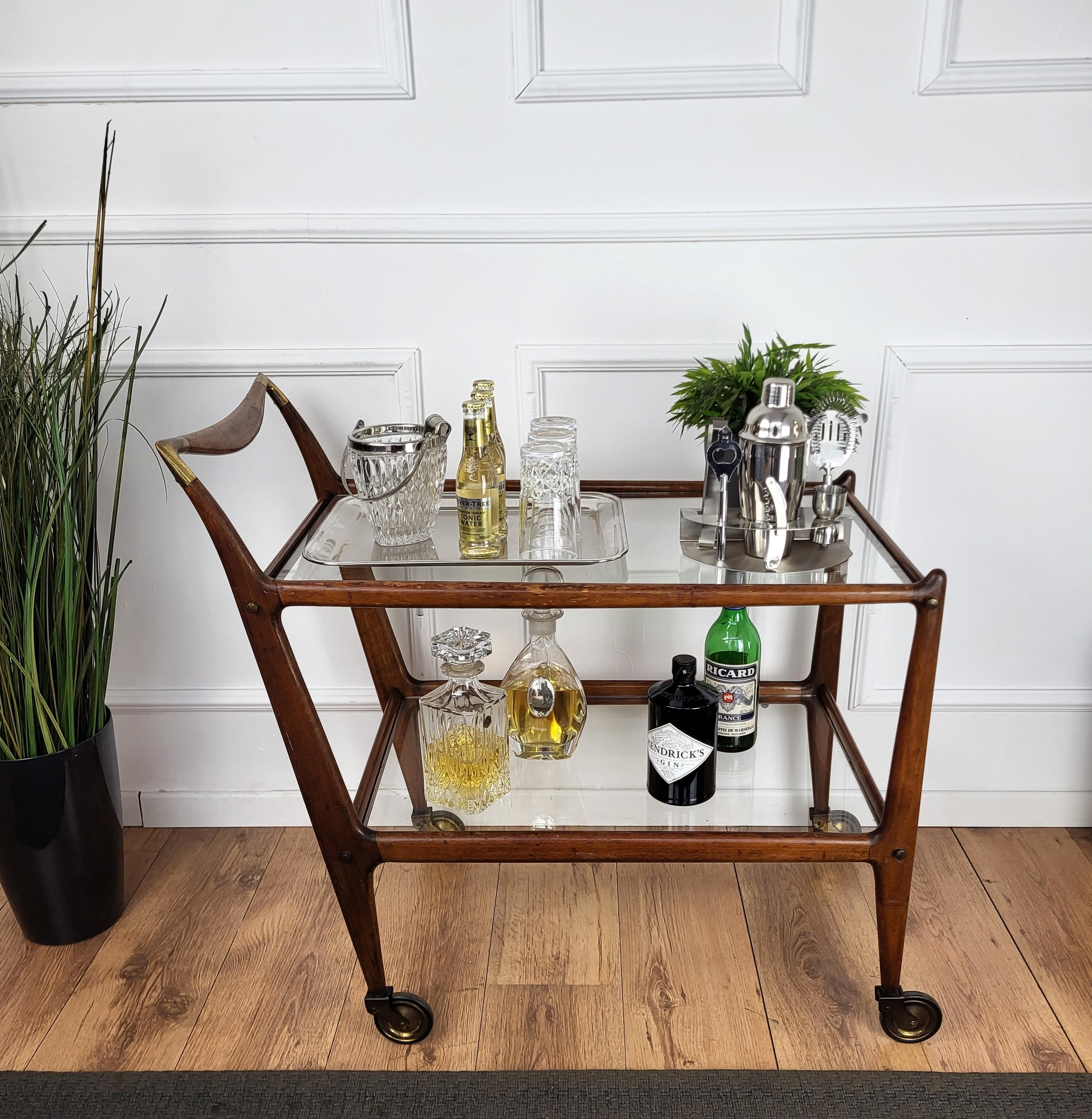 Unique and very elegant bar cart designed by Ico Parisi around the mid 1950s with two glass tiers and highlighted by the great wooden structure design and overall shape completed by the brass details of the handle corners and wheels. Created for the