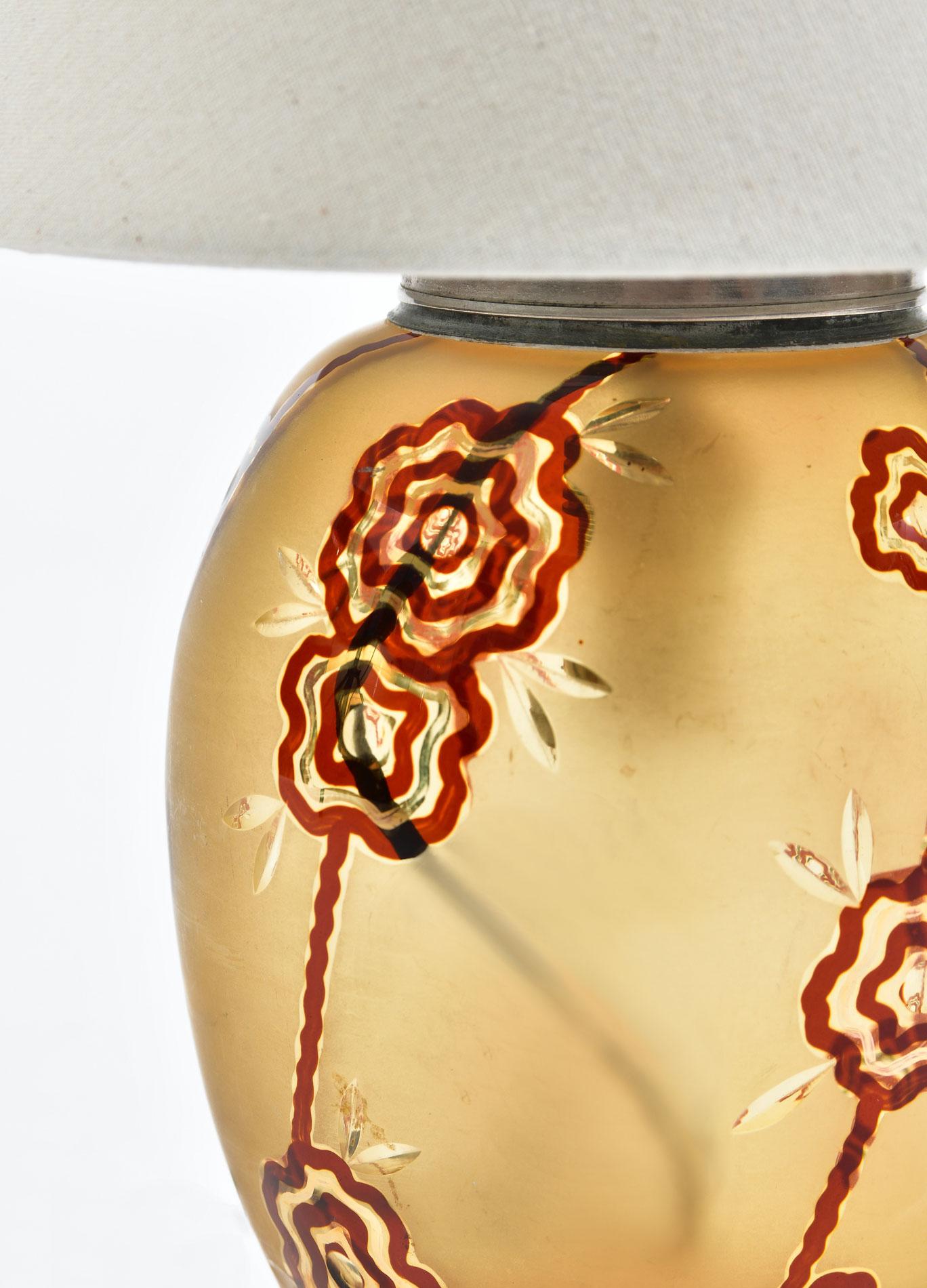 Rich amber glass base with red flower and etched leaves detail. A bulb inside the glass base throws a soft moody light.