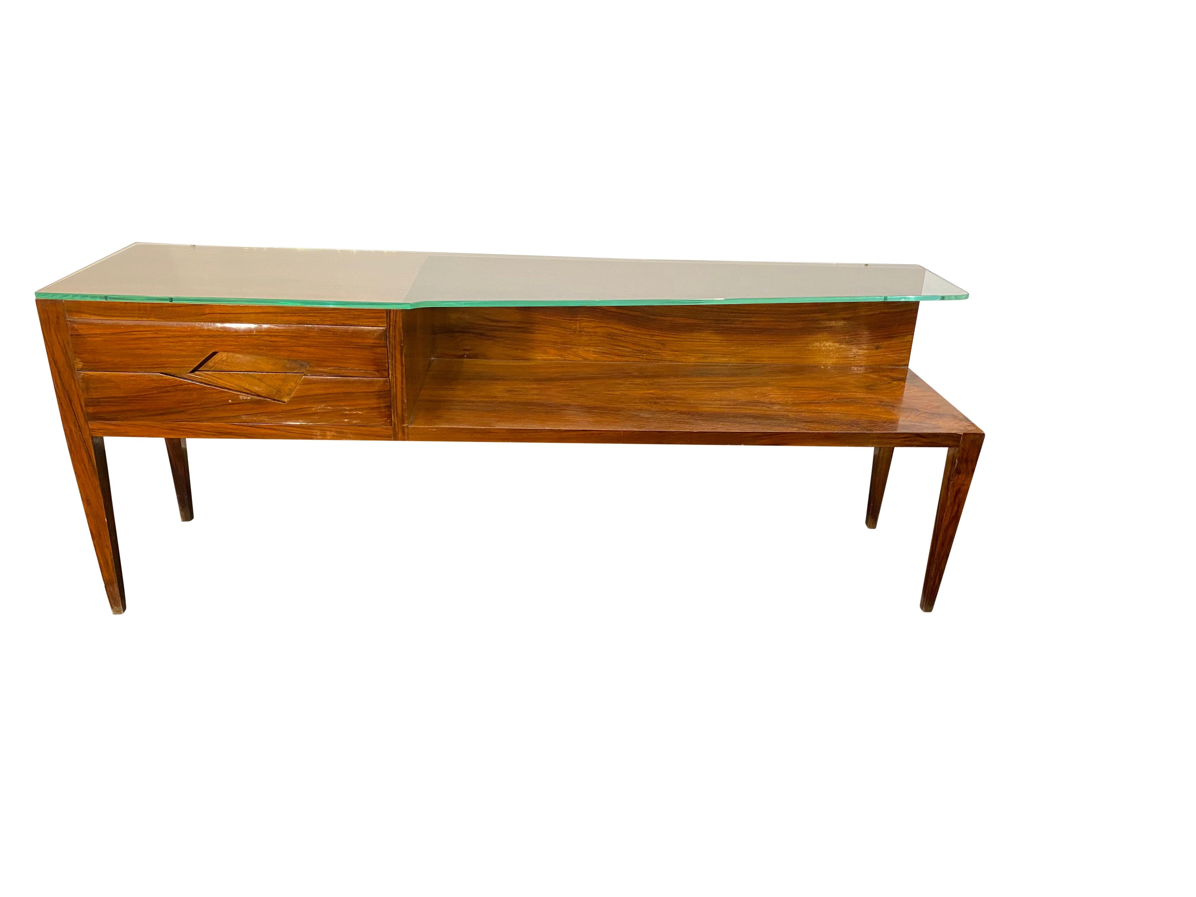 An architectural low Italian console table in cherrywood and angular glass featuring 2 single drawers and a shelf for display.

  