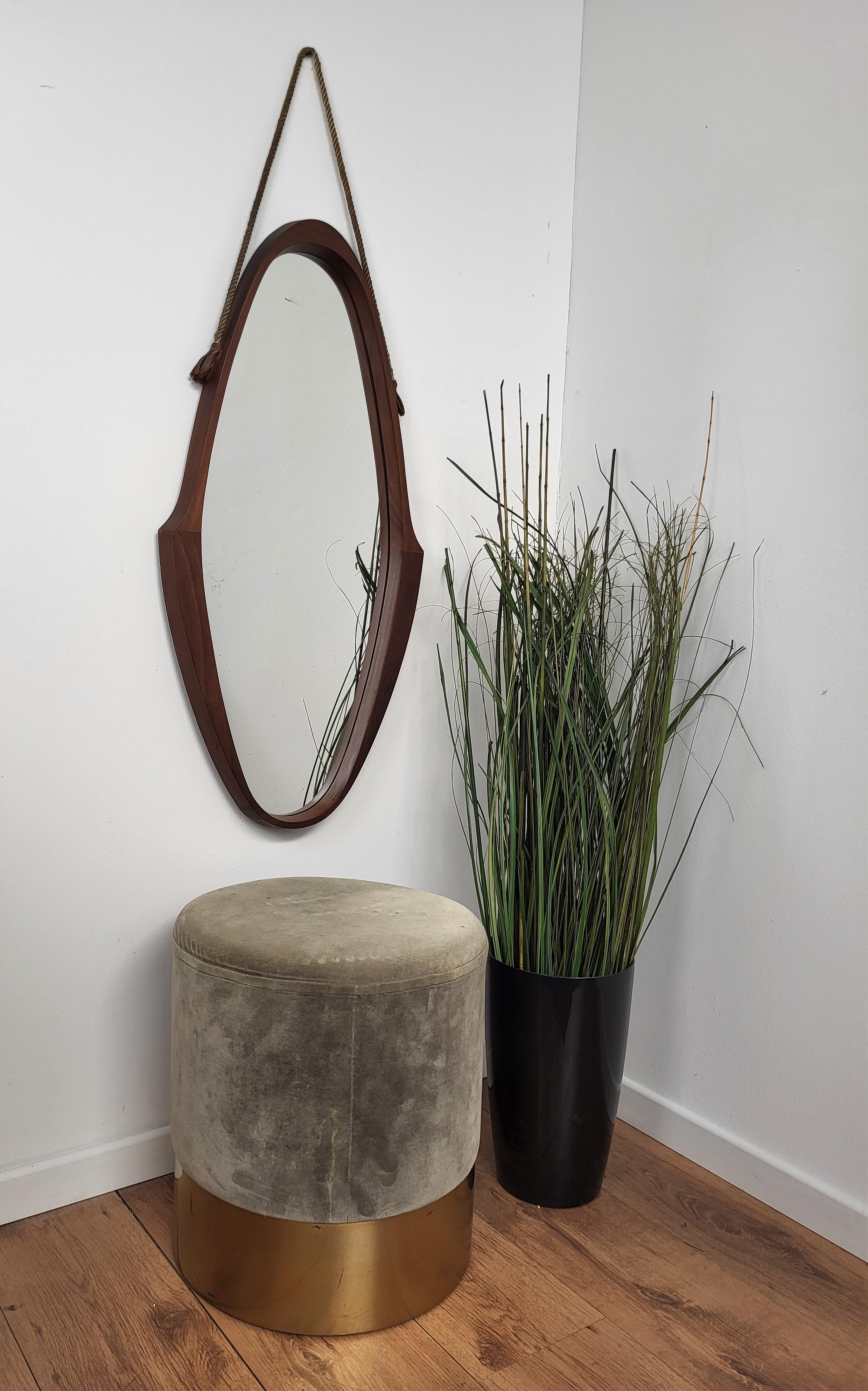 A Mid-Century Modern wooden oval wall mirror with rope and leather hanger, designed and produced in Italy, c. 1950s.
