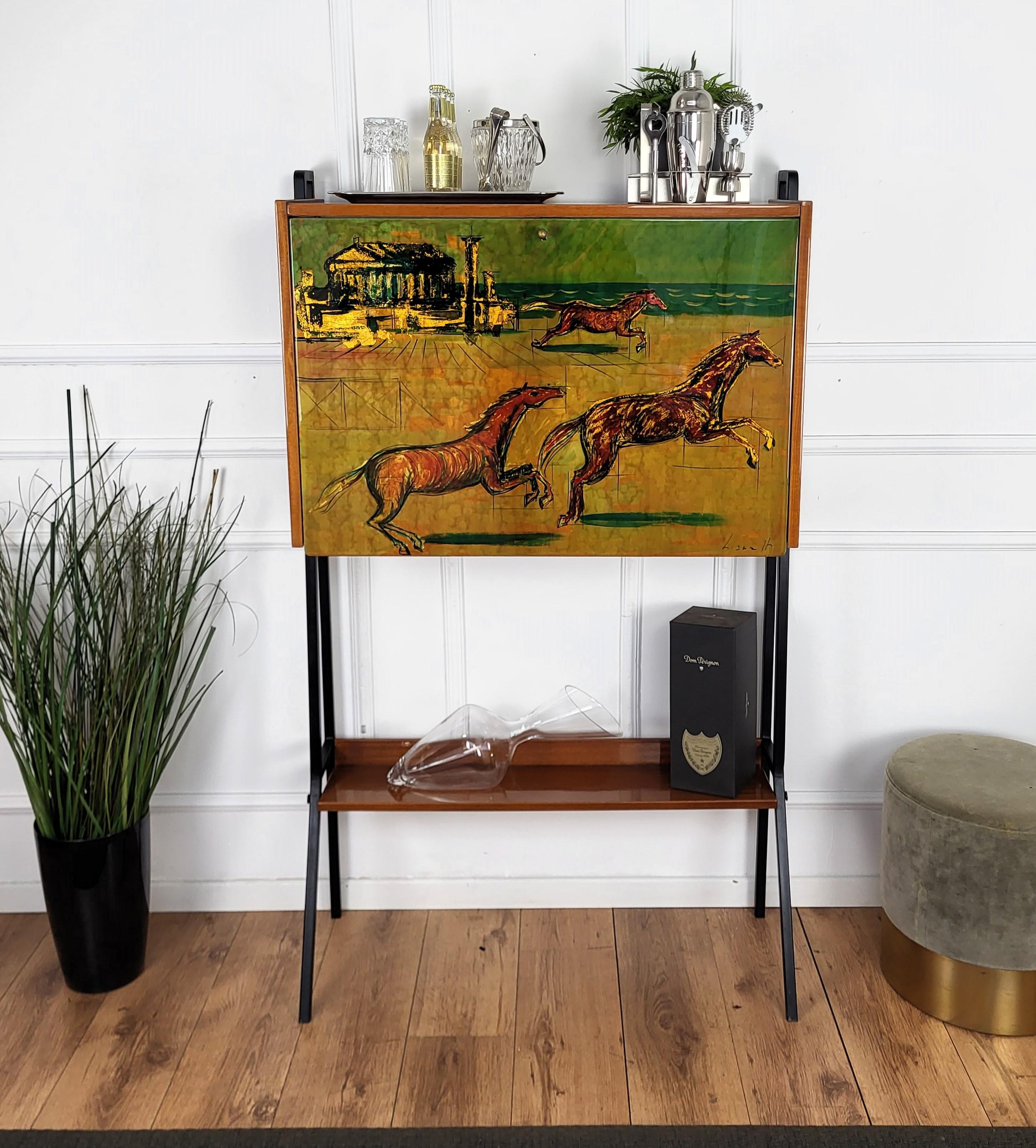 Very elegant Italian Mid-Century dry bar cabinet, with typical black metal side legs and top horses country theme decorated slant front door in wood and brass details. 
