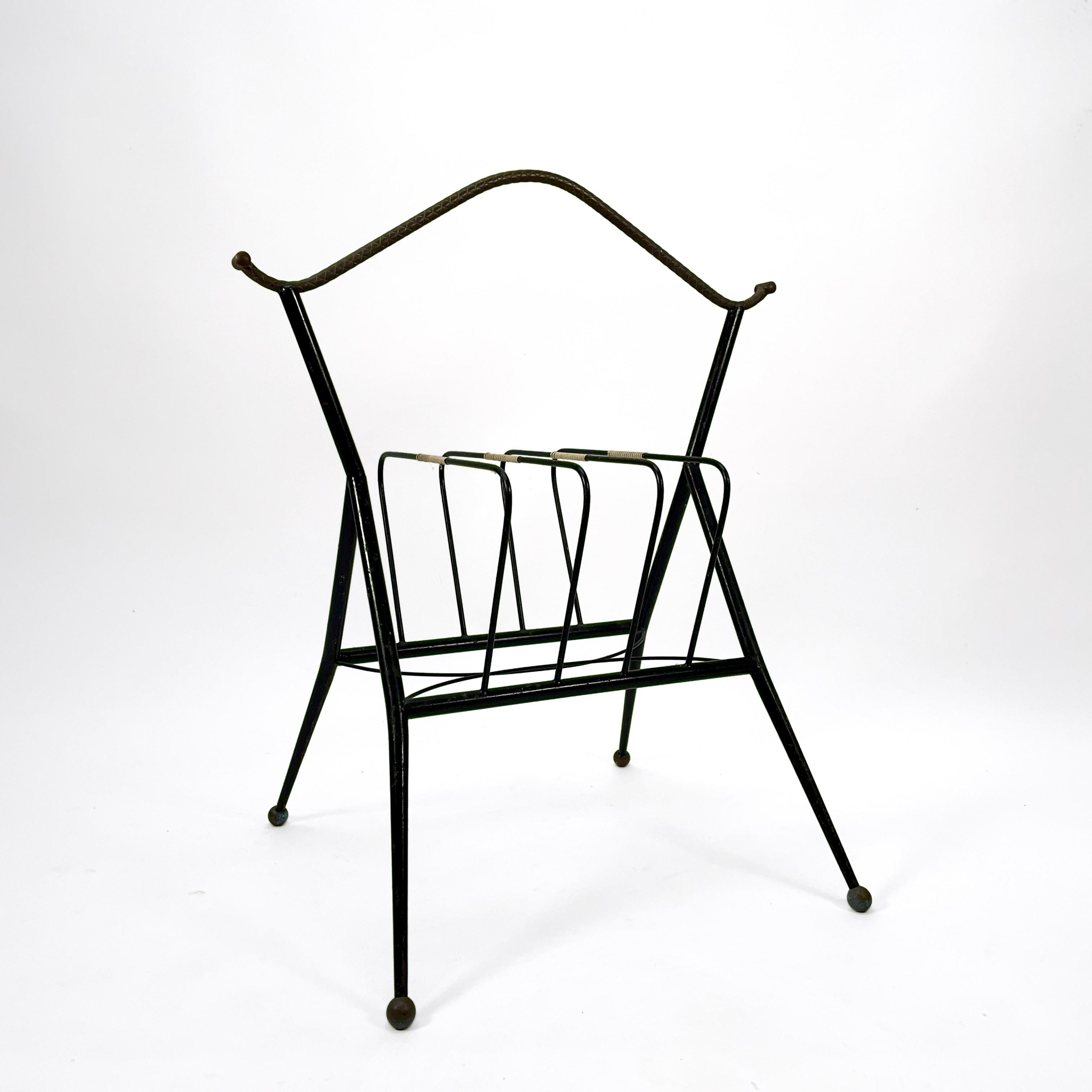 Elegant italian mid-century modern vintage magazine rack from the 1950s. 
This attractive and practical accessory consists of a black lacquered metal frame with beautiful brass details. A very charming piece of furniture that will suit any