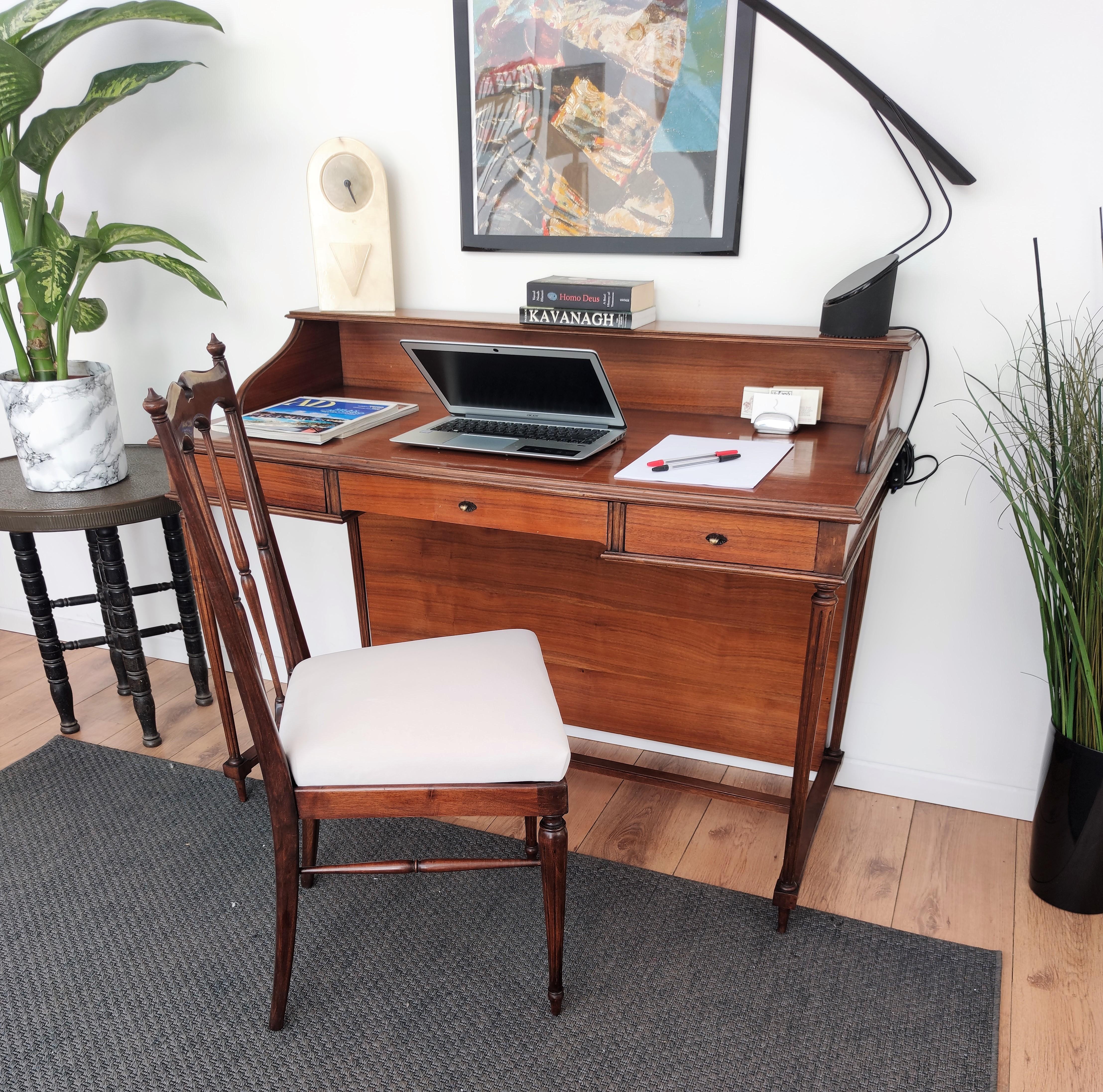 Beautiful and neoclassical midcentury Regency Italian writing table or desk with its paired newly upholstered chair both supported by elegant turned and fluted legs ending with tapered toupie feet, conjoined by an H-shaped stretcher. The desk
