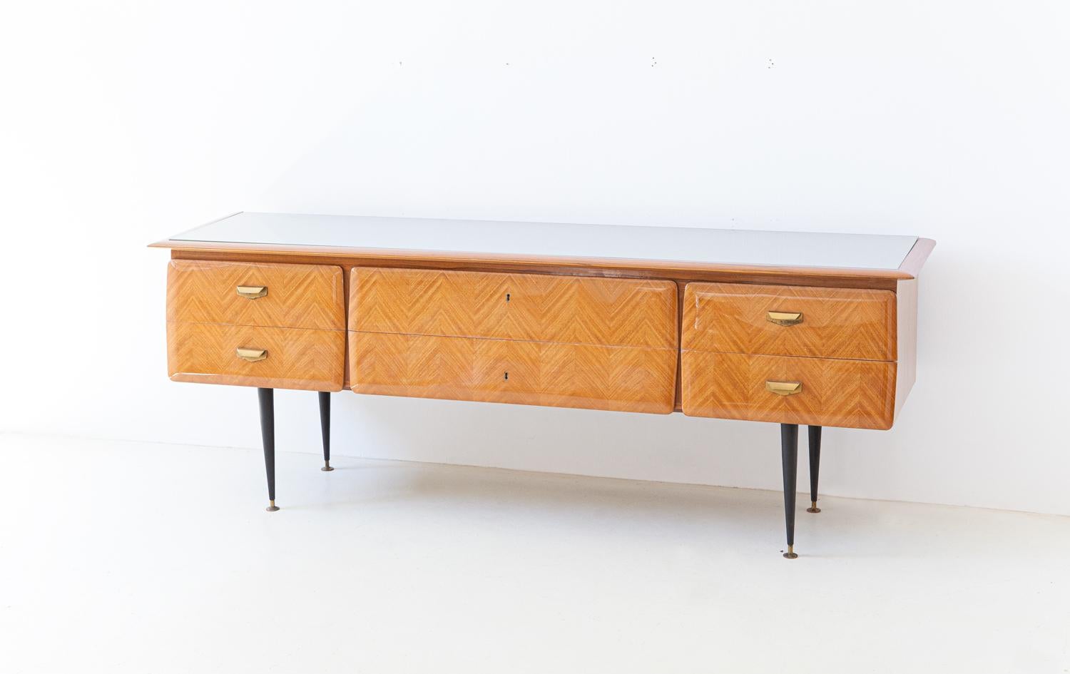 Elegant and modern sideboard from the 1950s
High quality Italian manufacture made by ‘furniture manufacturer in Cantu’
Blonde mahogany veneer, laid with dovetail work on the front.
Upper top in gray / silver back-lacquered glass
Brass handles and