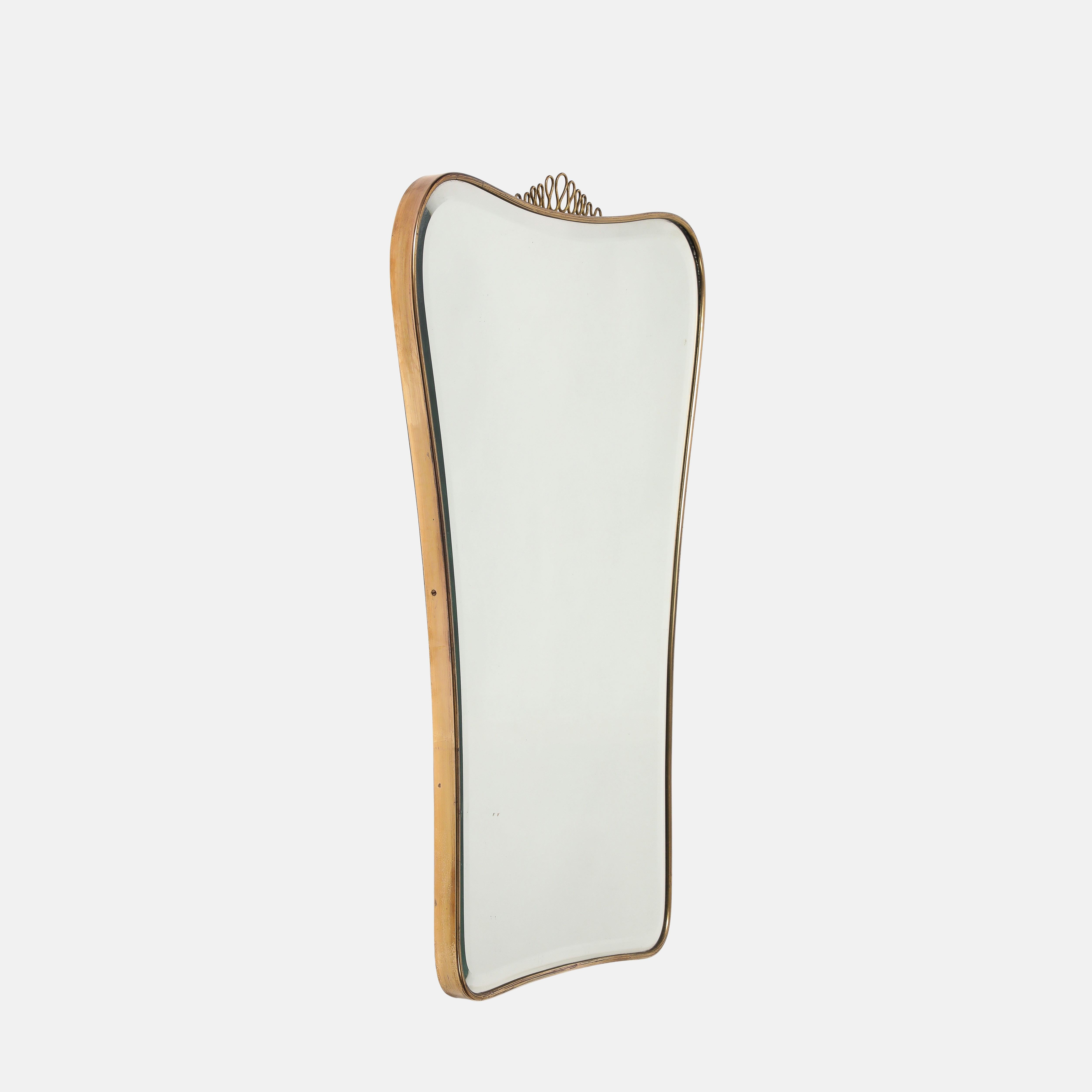 Miroir biseauté en laiton de style moderniste italien des années 1950, avec un élégant élément central de volute décorative en laiton, sur une partie supérieure légèrement arquée et incurvée allant en s'amenuisant vers la partie inférieure incurvée,