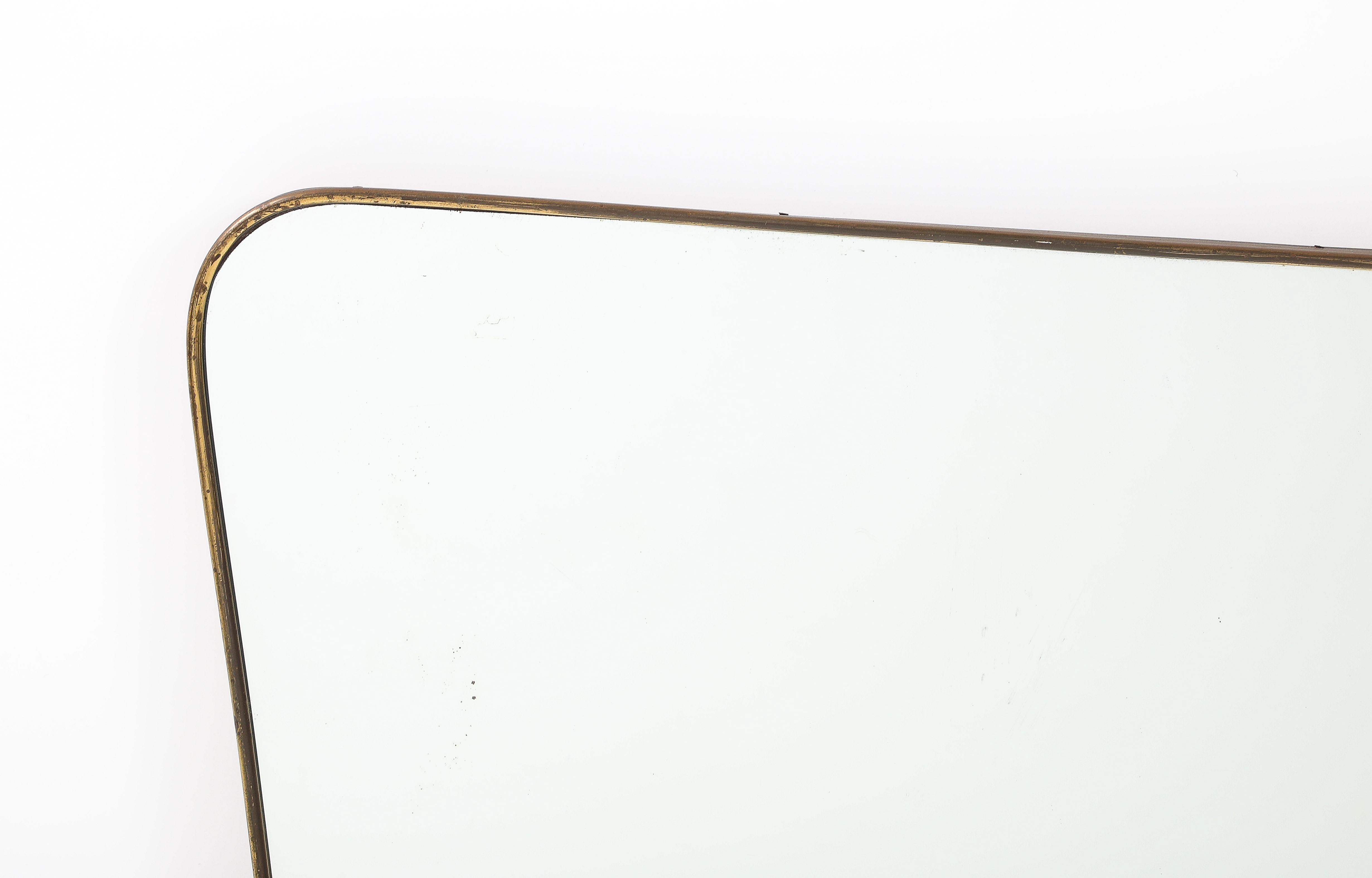 1950s Italian modernist horizontal overmantal brass mirror in the style of Gio Ponti.  This exquisite mirror has a gently curved brass frame with rounded corners and gently tapering sides, The is a central top decorative brass scroll element, and a