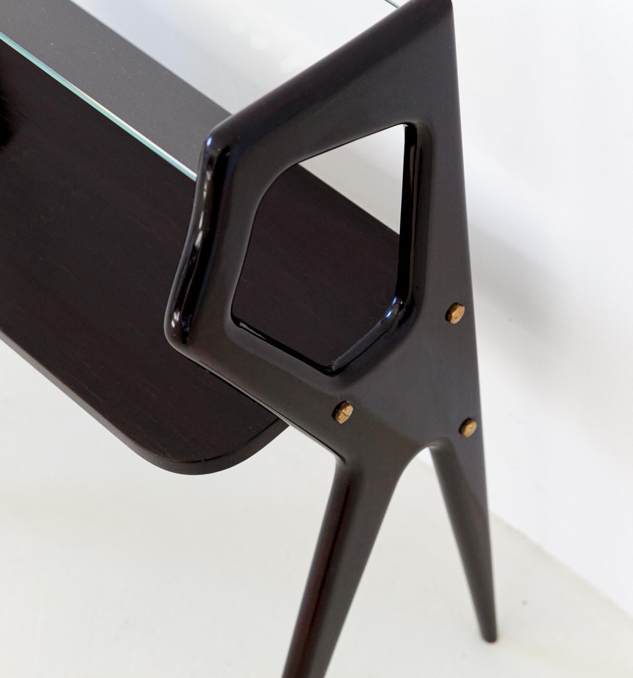 A sculptural and airy little console tables manufactured in Italy during the midcentury.
Made of dark dyed mahogany wood, clear glass and brass details.

Can be used as a side or bedside table.


       