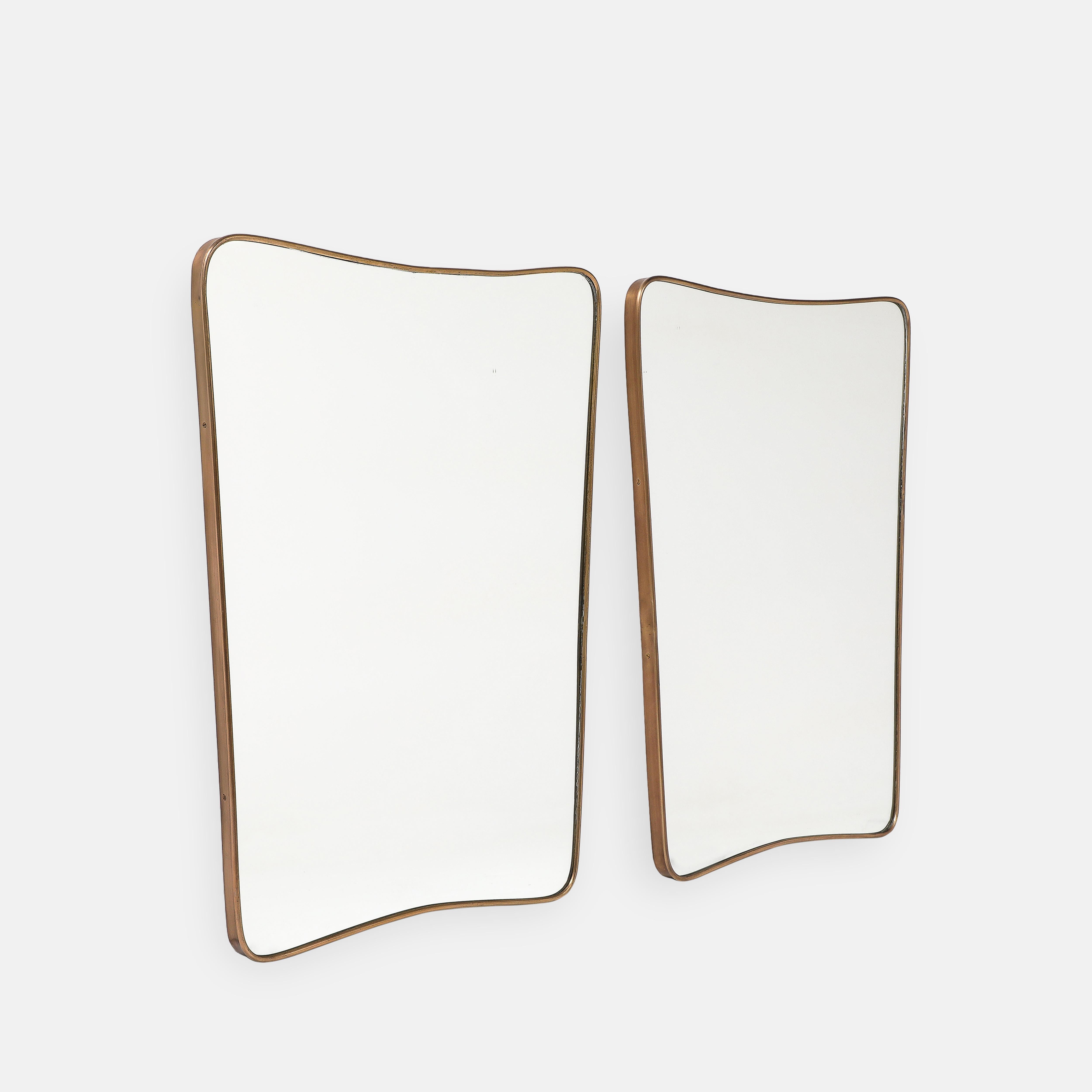 Paire de miroirs muraux modernistes italiens des années 1950, composés de cadres en laiton de forme arrondie avec des sommets légèrement arqués et des coins arrondis qui se rétrécissent vers le bas, avec des supports en bois. Les plaques d'origine