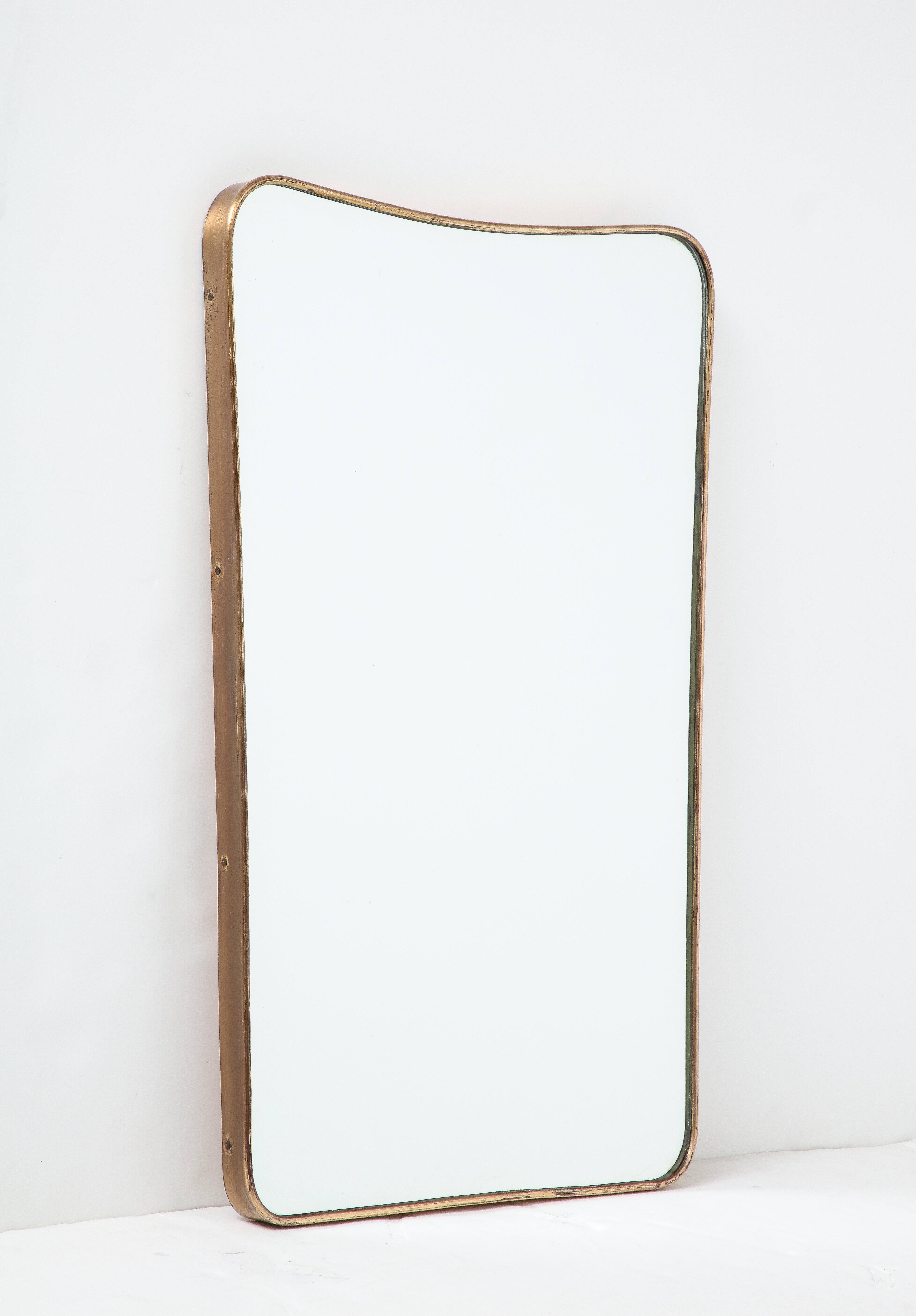 Miroir mural en laiton de forme moderniste italienne du milieu du siècle dernier, avec un joli dessus incurvé et des coins légèrement arrondis, et un verre miroir d'origine, années 1950. Cet élégant miroir d'époque présente une belle patine vieillie