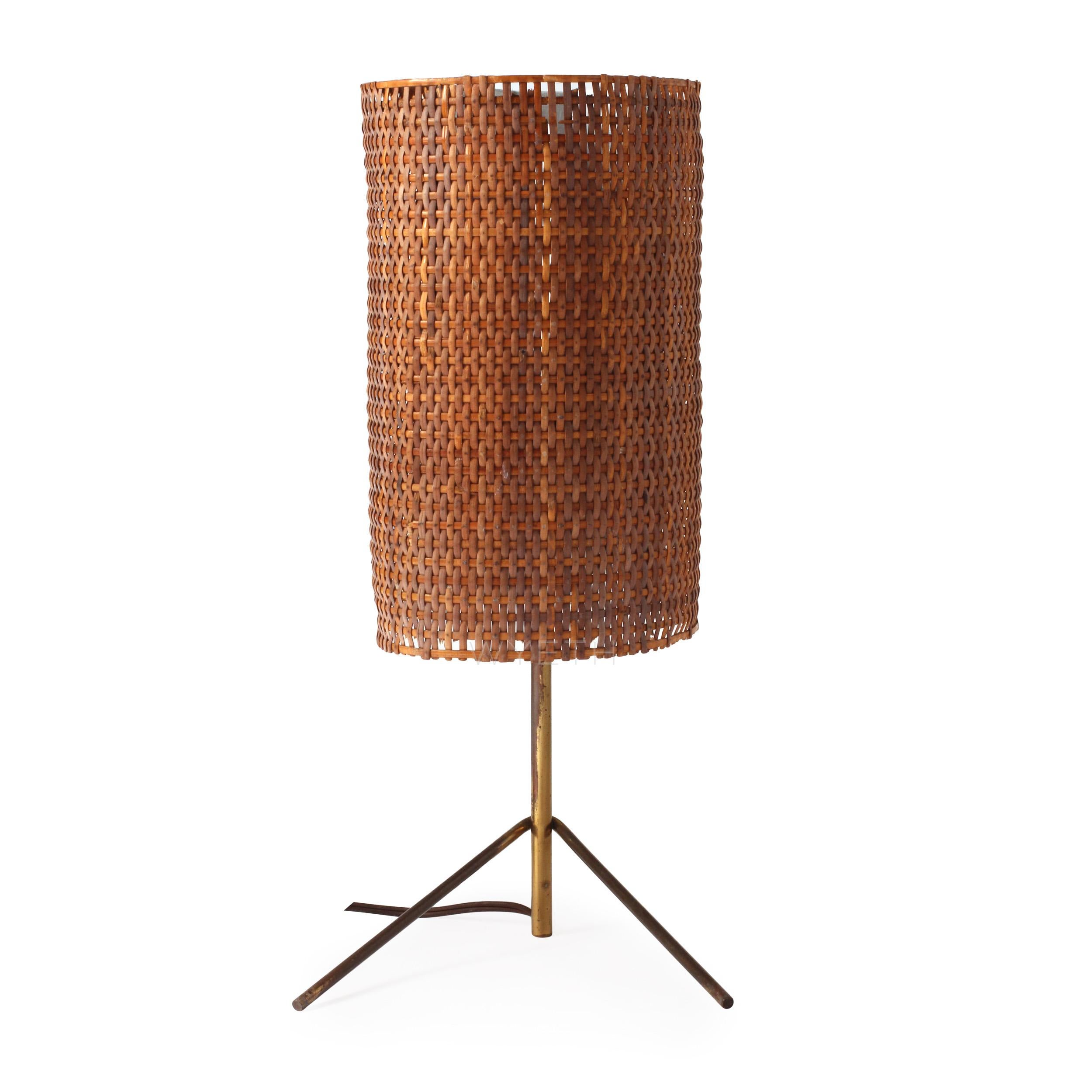An unusual and expressive table lamp having a spare three-point brass base supporting a lacquered steel and cane shade.