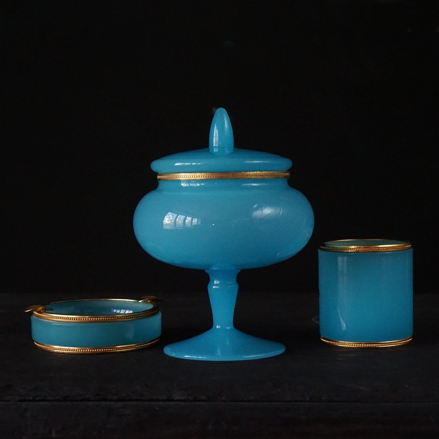 1950s set of three blue opaline glass items. Made in Italy 
The bright blue milk, opaline or cased glass is heavy and thick, all items have a decorative ormolu brass mount or rim

The set consists of an ashtray a small jar, probably for holding