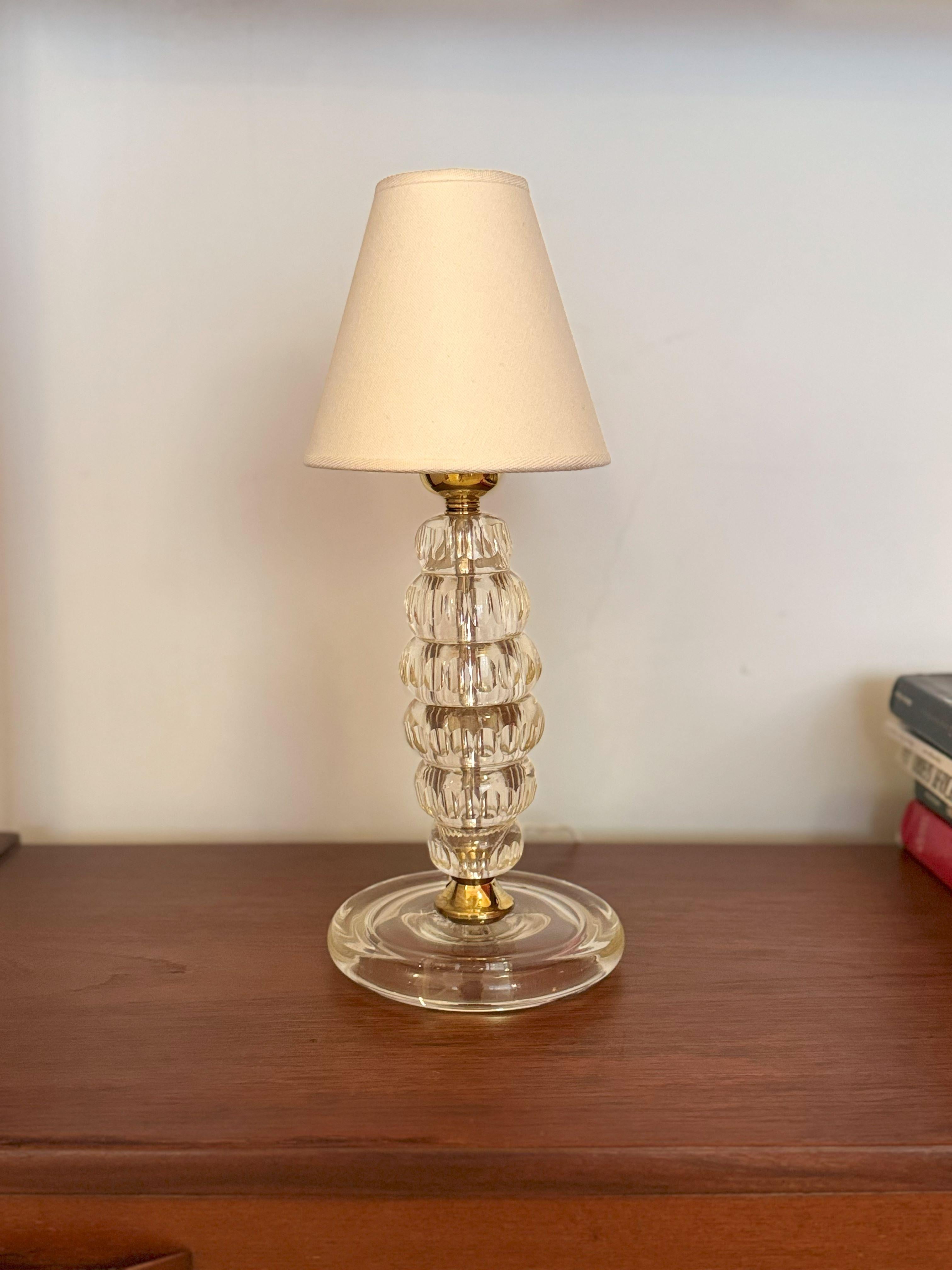 Fabriquée à la main à Murano, en Italie, dans les années 1950, cette petite lampe de table élégante présente une colonne empilée de rondelles de verre clair soufflées au moule. 

Les éléments en laiton poli à la base et au col offrent un contrepoint
