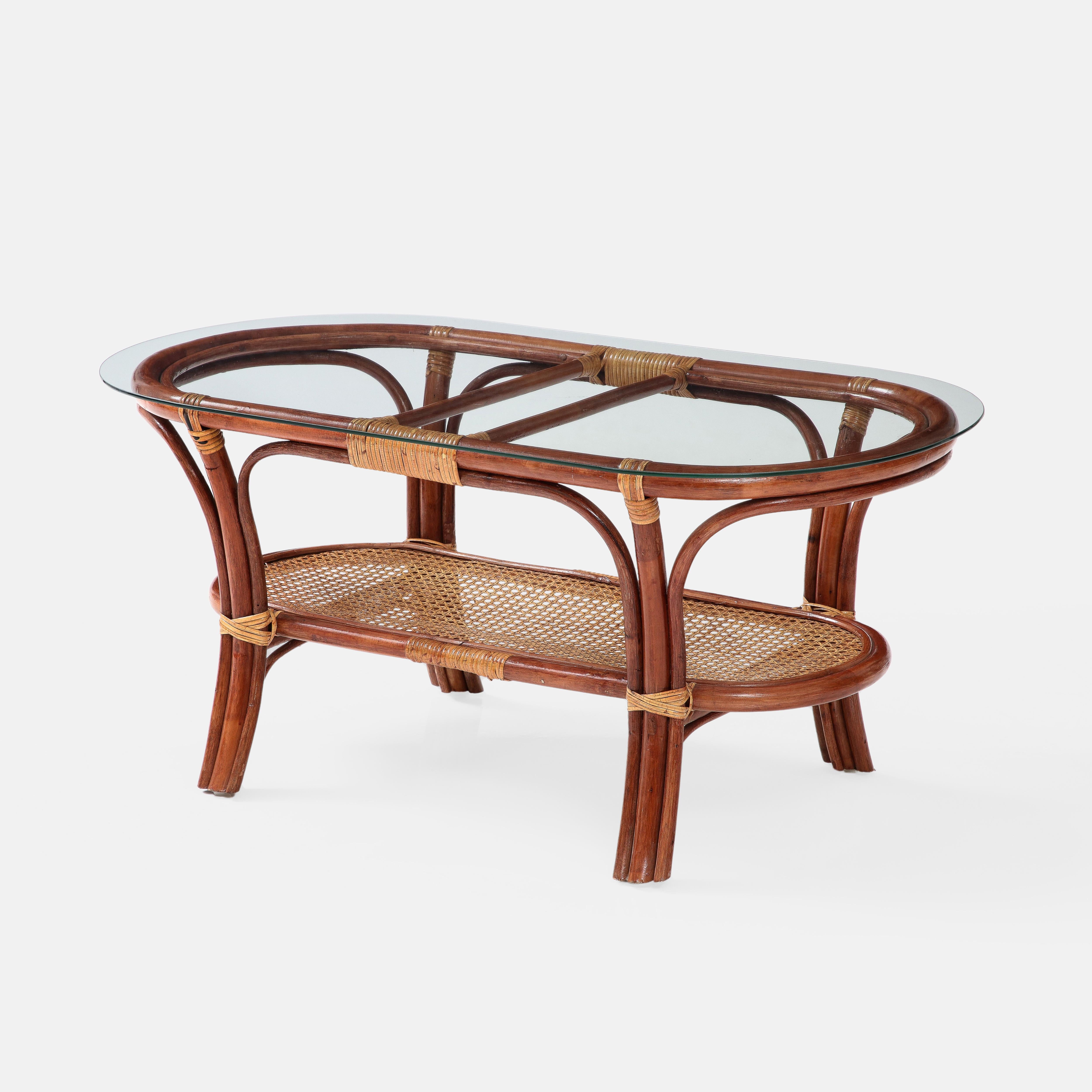 1950s Italian oval two-tiered coffee table in bamboo and rattan with glass top and Vienna straw lower tier shelf. This rarely seen vintage handmade oval coffee table exudes elegance and charm in all the wonderful details. The organic bamboo frame is