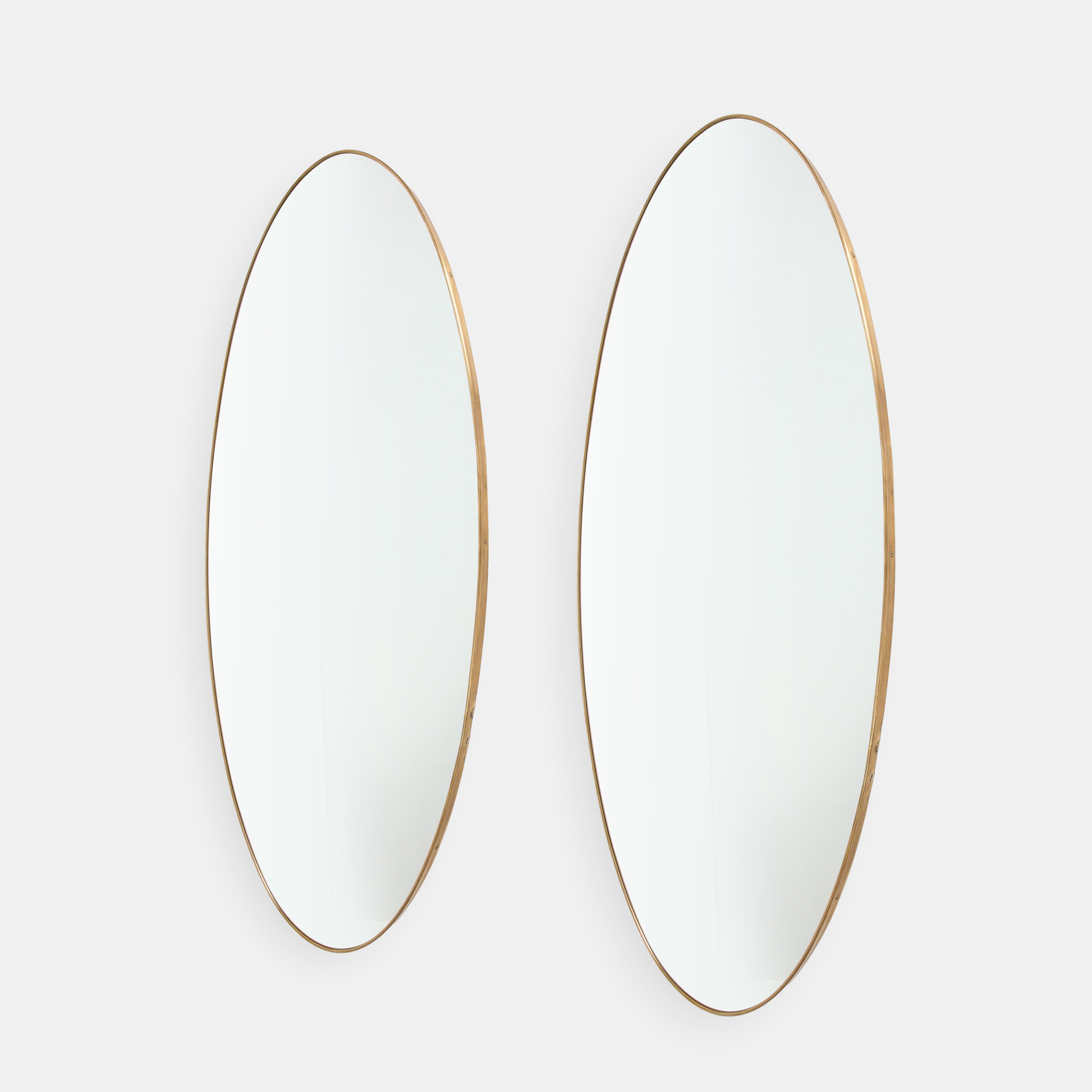 1950s Italian rare pair of grand scale oval wall mirrors. These elegant mirrors are large and striking in size and have a beautiful rich patinated shaped brass frames and solid construction with wood backing. This monumental size brass mirror is
