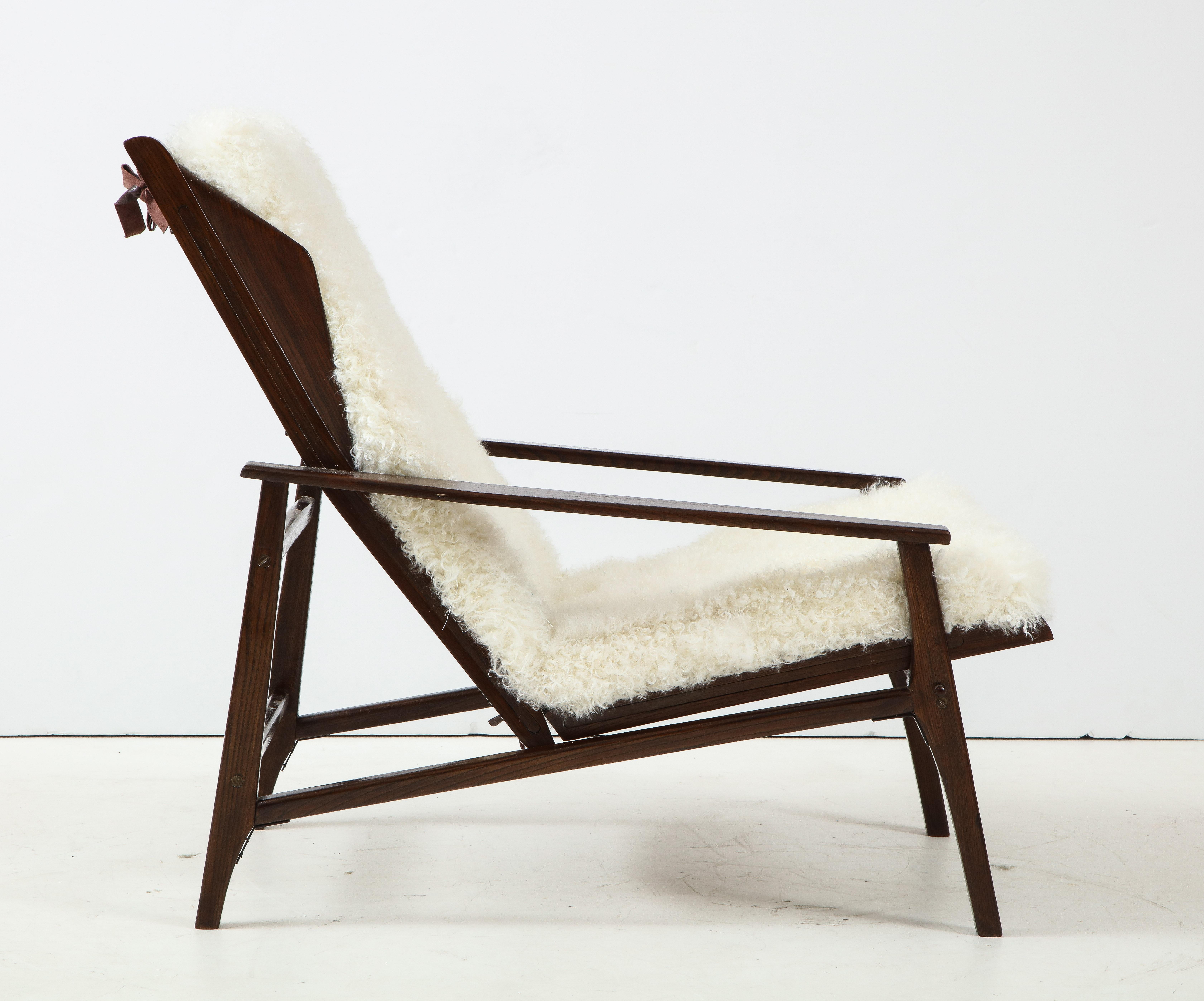 1950s chic Italian reclining lounge chair with stained oak frame and back and seat cushions upholstered in a luxurious white Kalgan lambskin.  This lounge chair can be adjusted to different reclining positions. The Kalgan lambskin cushions have
