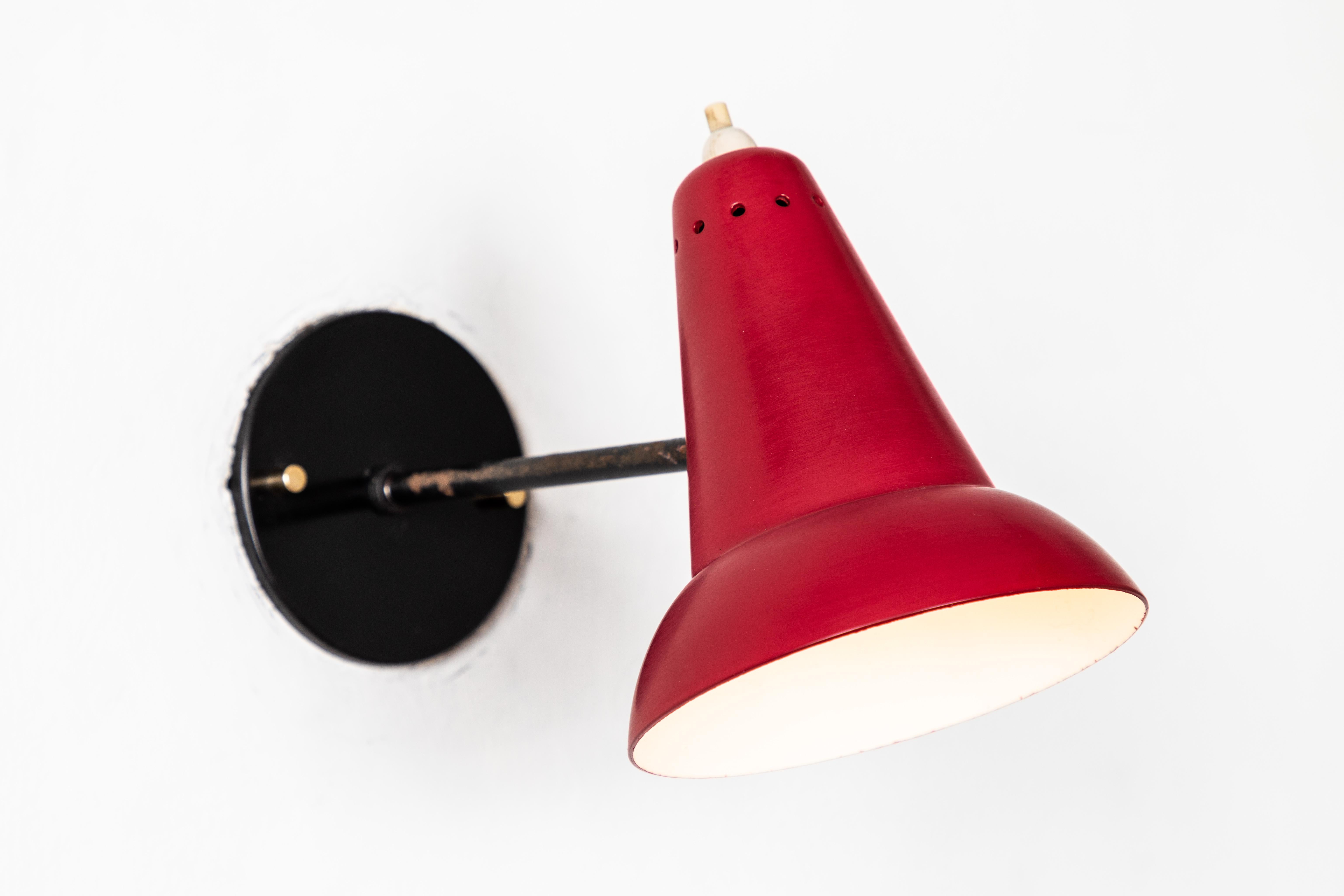 1950s Italian red articulating sconces attributed to Gino Sarfatti. Executed in brass and red painted aluminum. Sconces pivot up/down and left/right on a ball joint. Custom black backplates with brass hardware for hardwiring mounting over standard