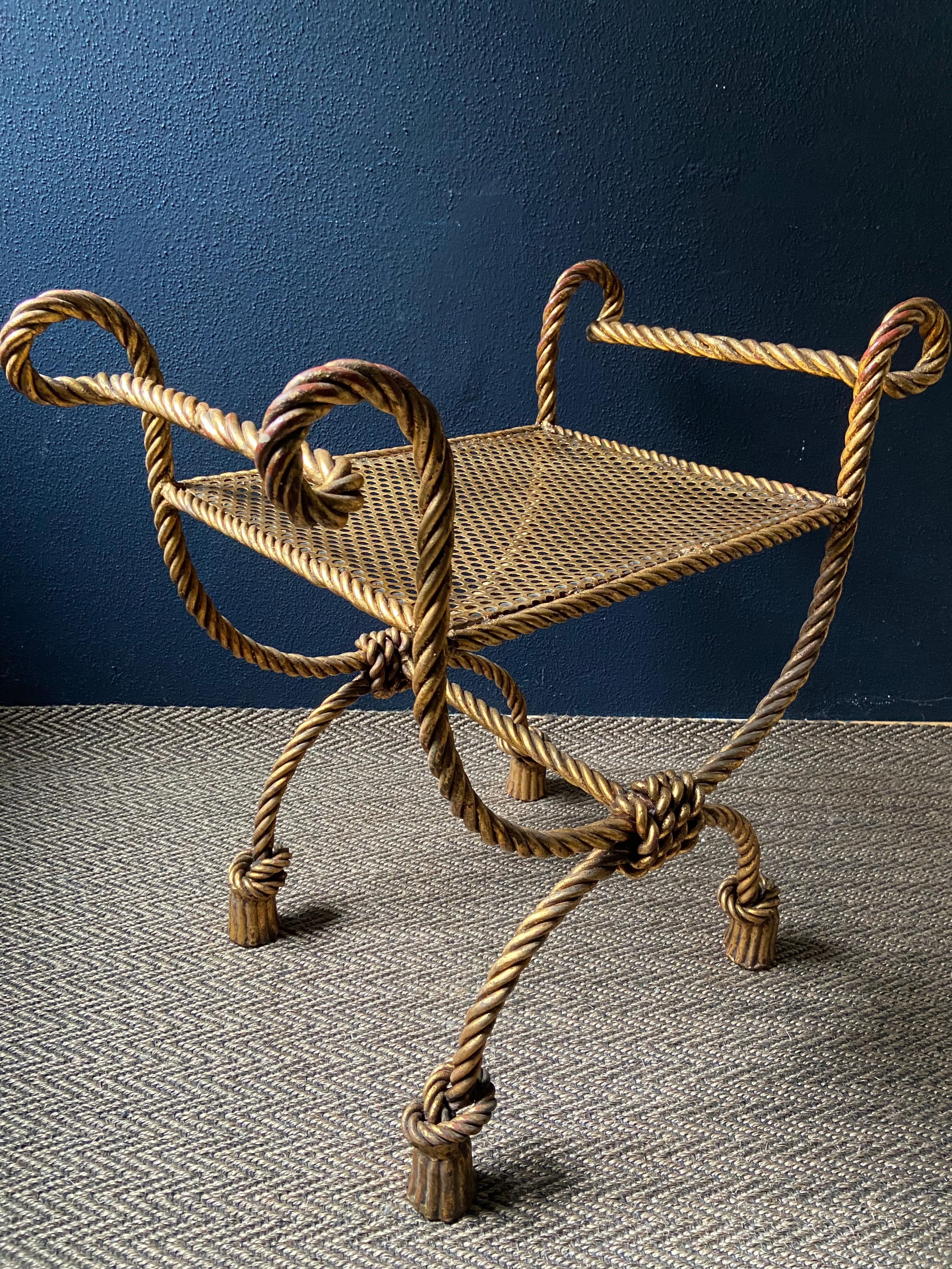 Questo sgabello Curule o Savonarola in ferro battuto dorato, con una struttura in corda ritorta e piedi con nappe, è un pezzo di Hollywood Regency italiana degli anni '50.

Questa seduta è perfetta come seduta per la camera da letto o per il bagno,