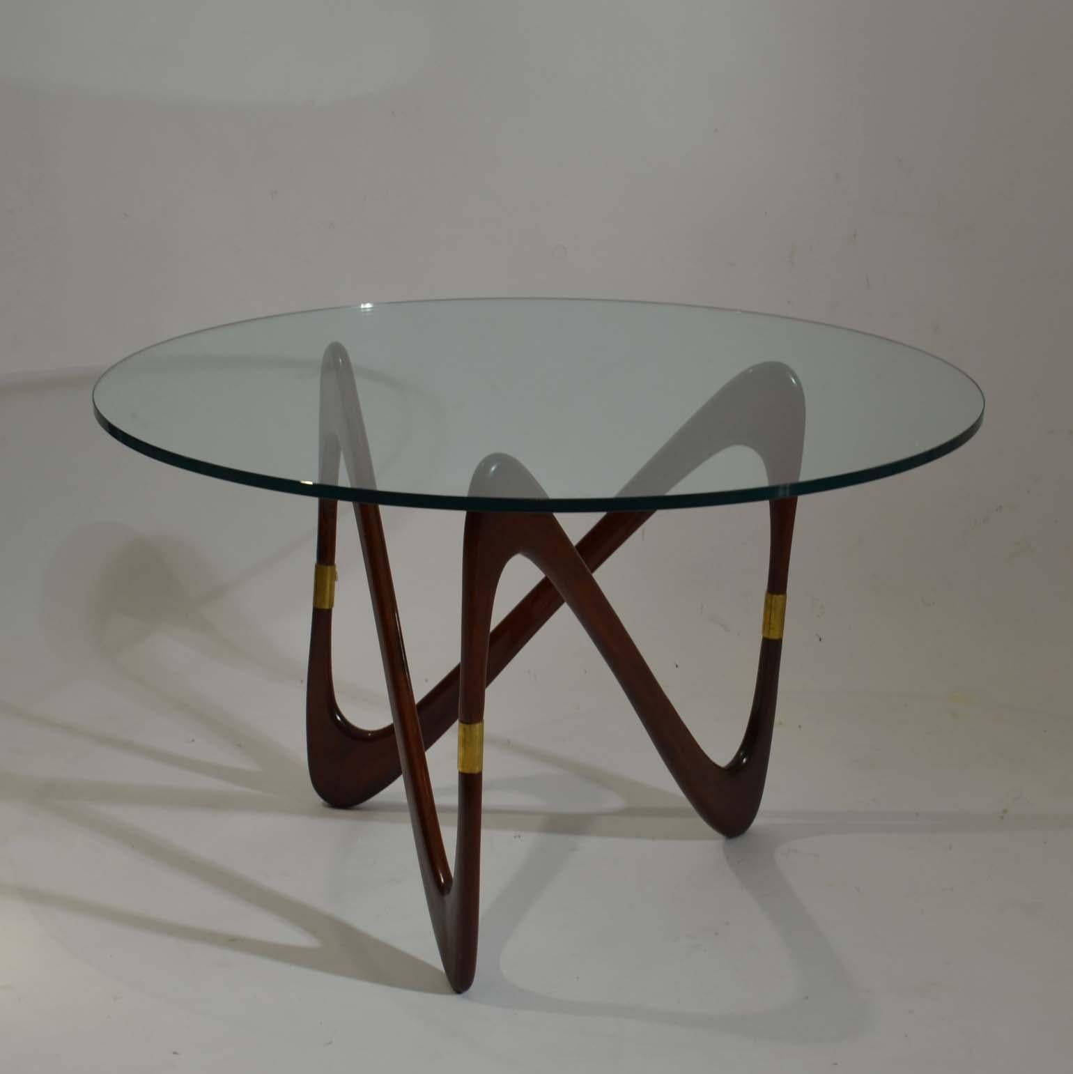 An Italian architect-designer Cesare Lacca created a series of modernist furniture and metalwork throughout the 1950s. This sculptural coffee table has an elegant flow of mahogany wood S-shape legs connected into a continual loop joined by three