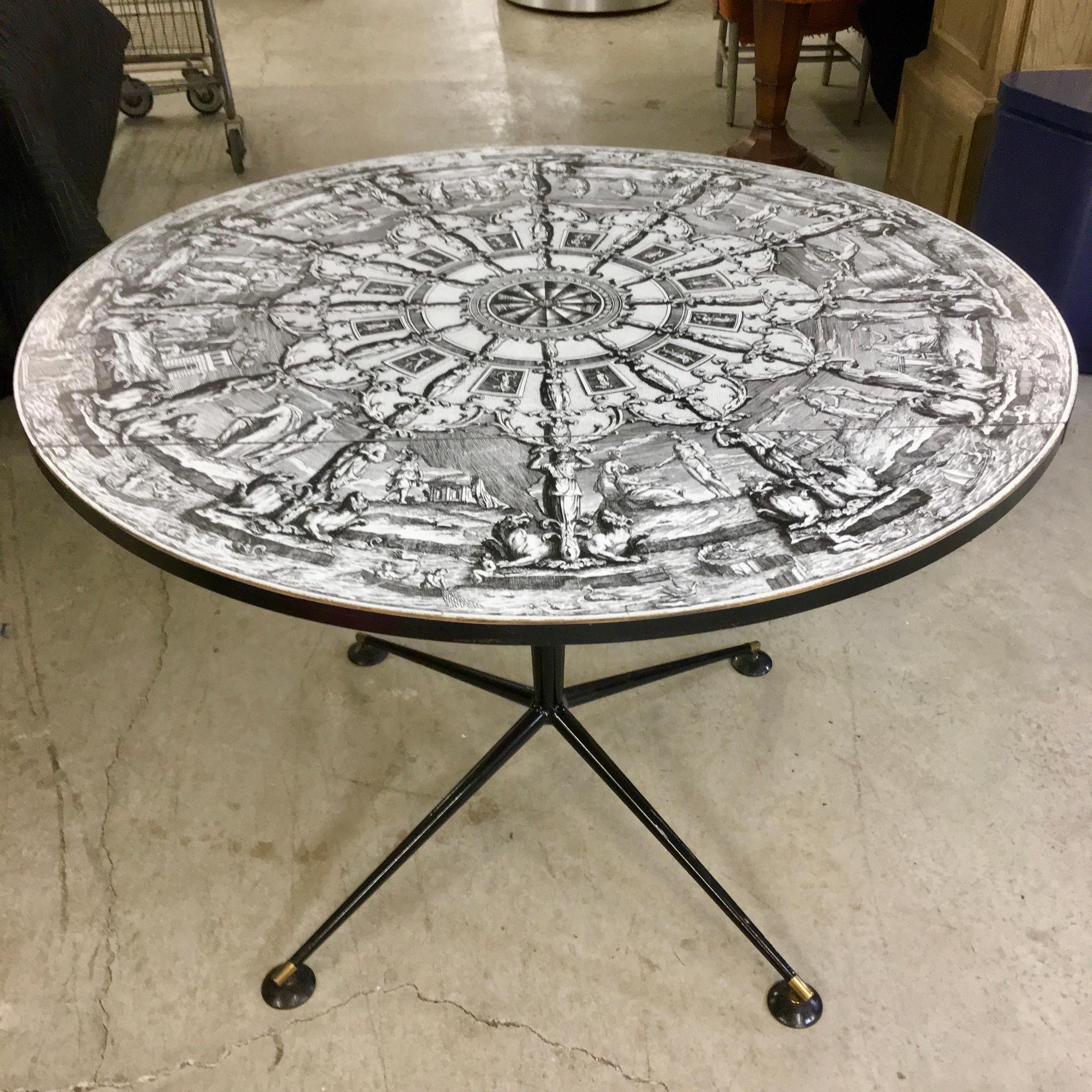 Vintage 1960s round double drop-leaf table top in style of Fornasetti, mounted on single slim tapered black enameled metal pedestal stem on four star splayed base, with brass sabots and round disk 'lunar landing pad' self-leveling feet designed by