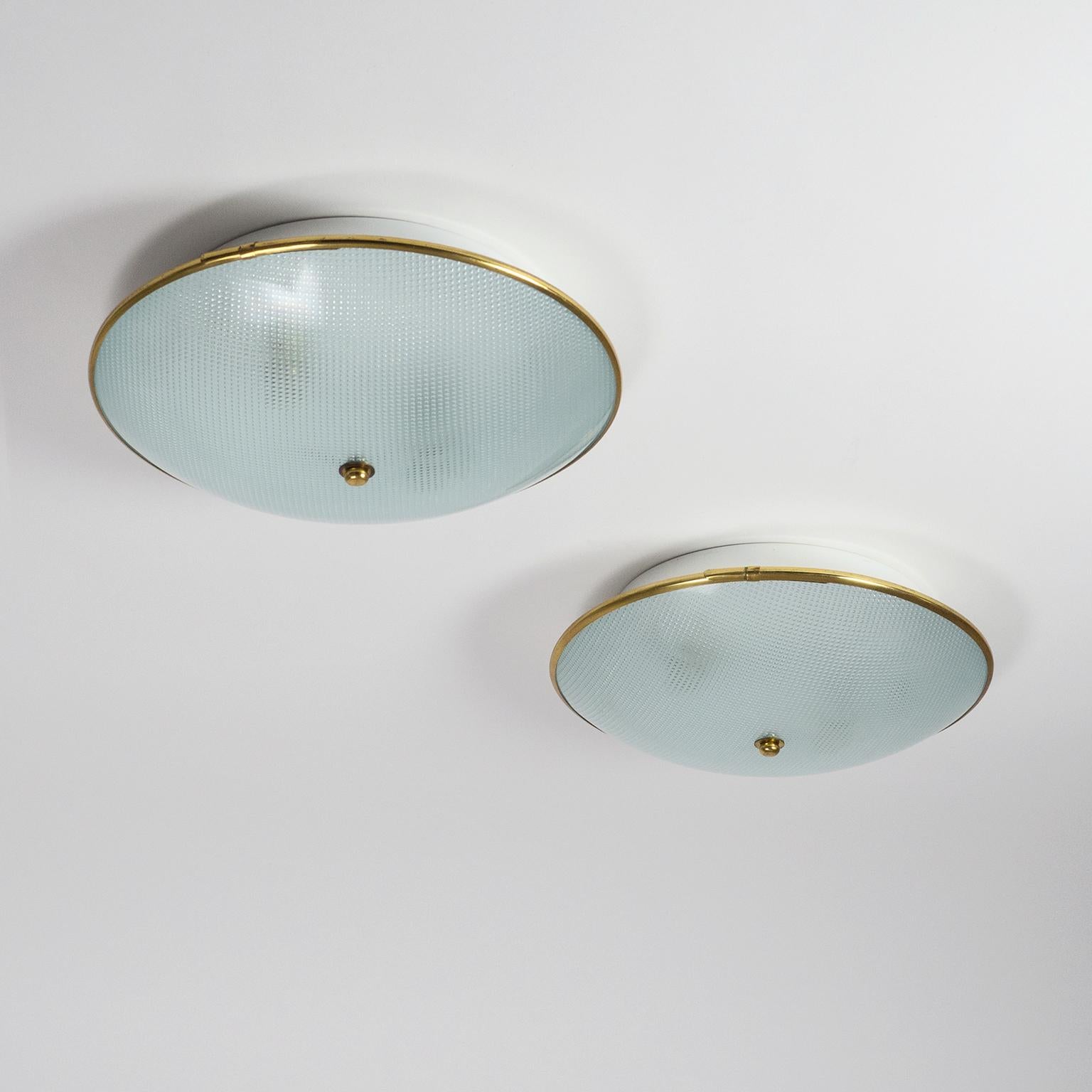 Modernist pair of Italian textured glass flush mount or wall lights from the 1950s. A white lacquered aluminum backplate houses two original brass and ceramic E14 sockets with new wiring. The glass diffuser has a geometric texture on the inside and