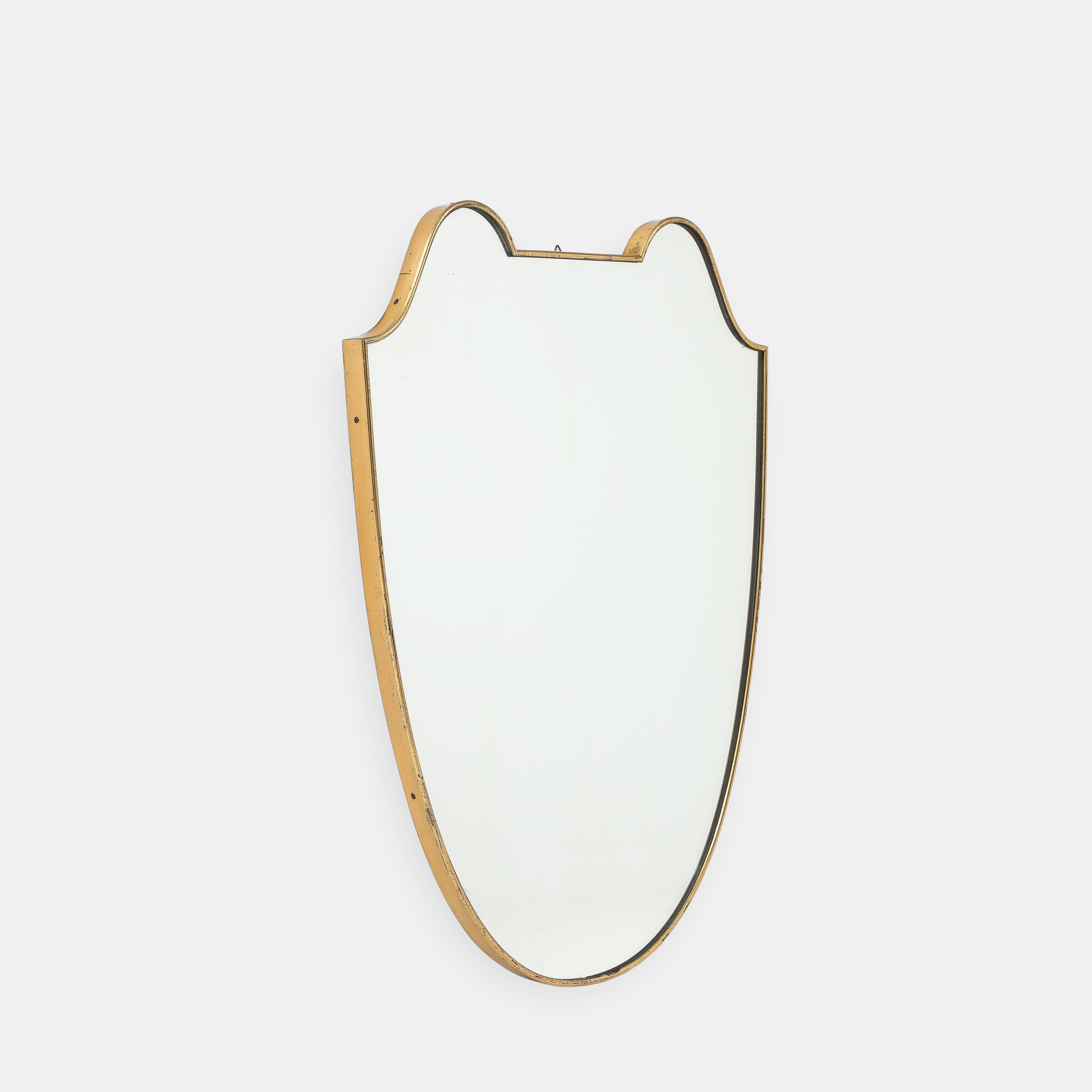 1950s Italian shield shaped brass wall mirror. This original midcentury period mirror has a lovely curved form and a beautiful rich patina to the brass with wood backing.