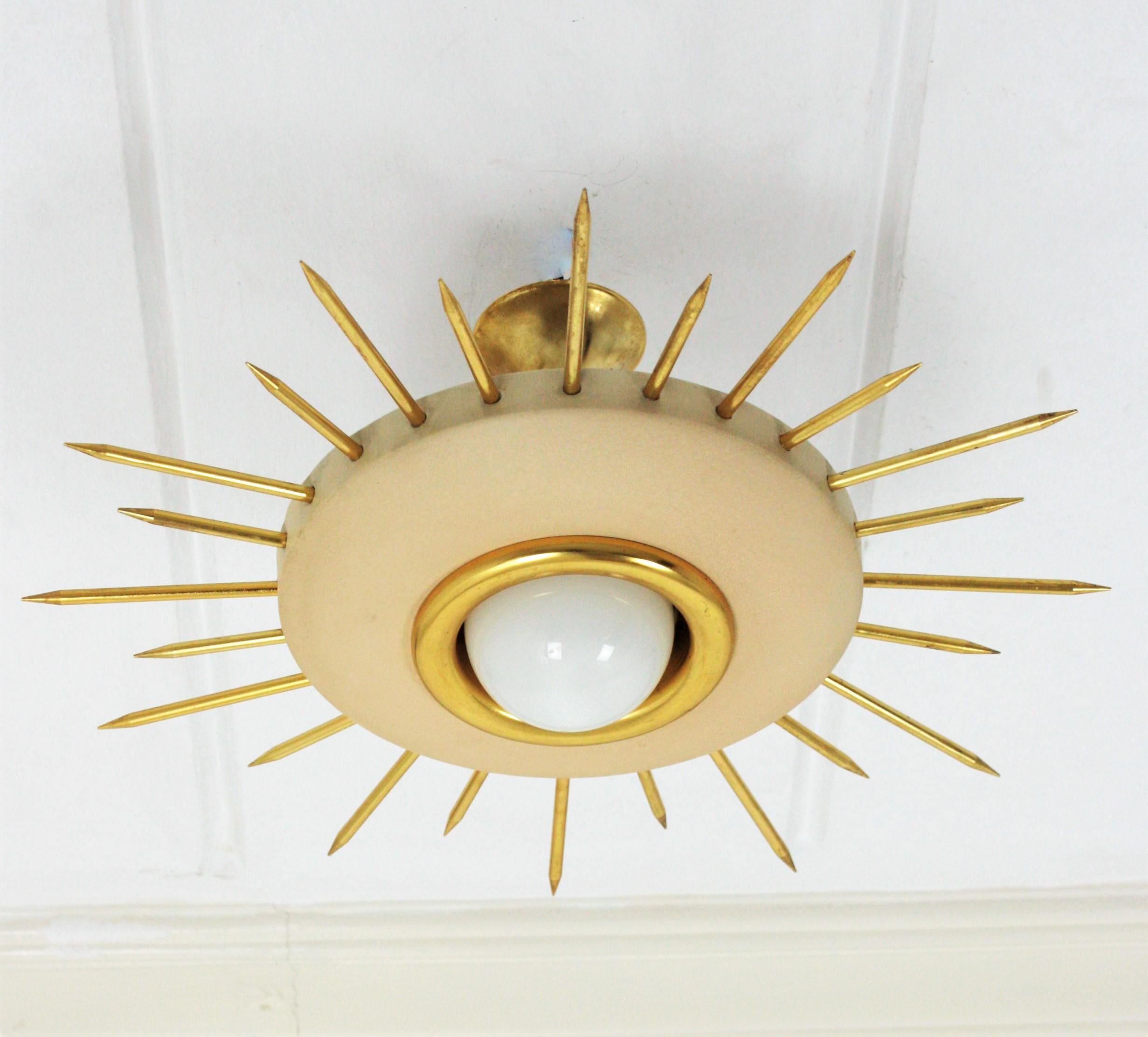 Mid-Century Modern beige lacquered and gilt metal sunburst light fixture, Italy, 1950s.
This eye-catching ceiling lamp features a beige metal shade surrounded by gilded thick rays in two sizes. It has a central light with a ring in gilt metal and a