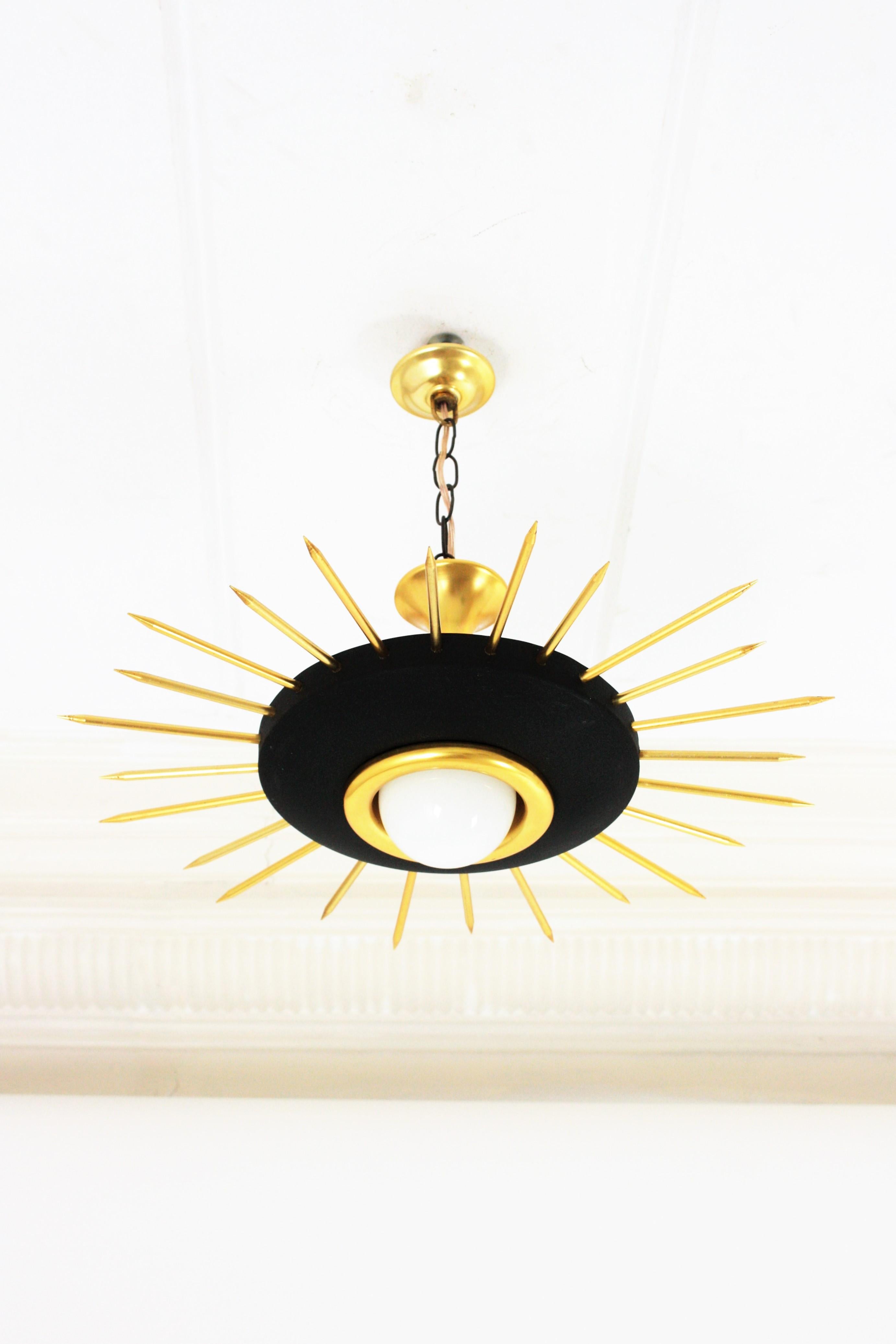 Mid-Century Modern BLACK metal and BRASS sunburst suspension light, chandelier or light fixture. Italy, 1950s.
This eye-catching ceiling lamp features a black lacquered metal shade surrounded by brass thick rays in two sizes. It has a central light