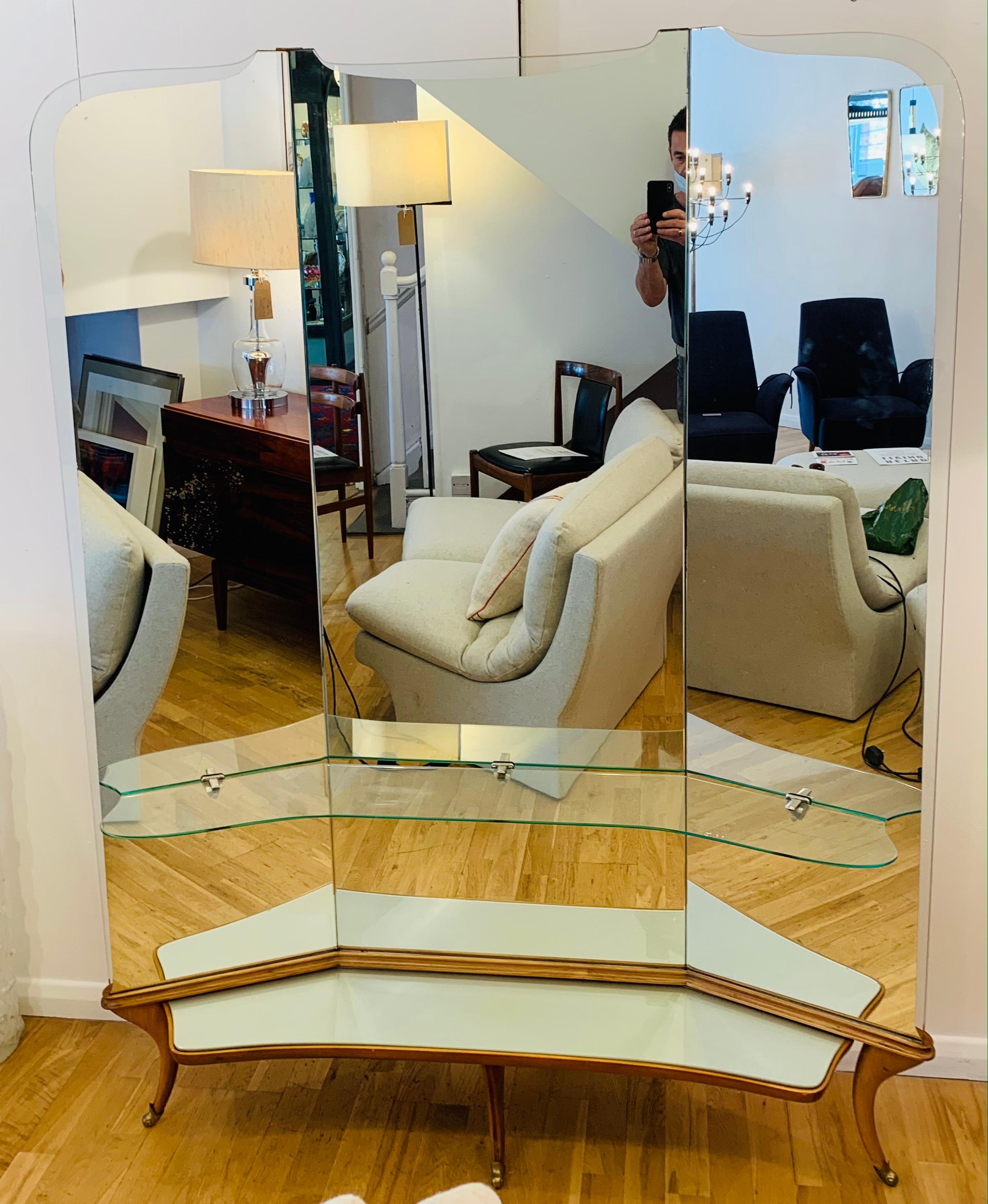 A large 1950s Italian triptych floor standing mirror. The mirror sits on three curved legs, with brass scrolled feature feet at the front, and two tapered stabilising feet at the back. Each of the three mirrors slot into the back of the base and are