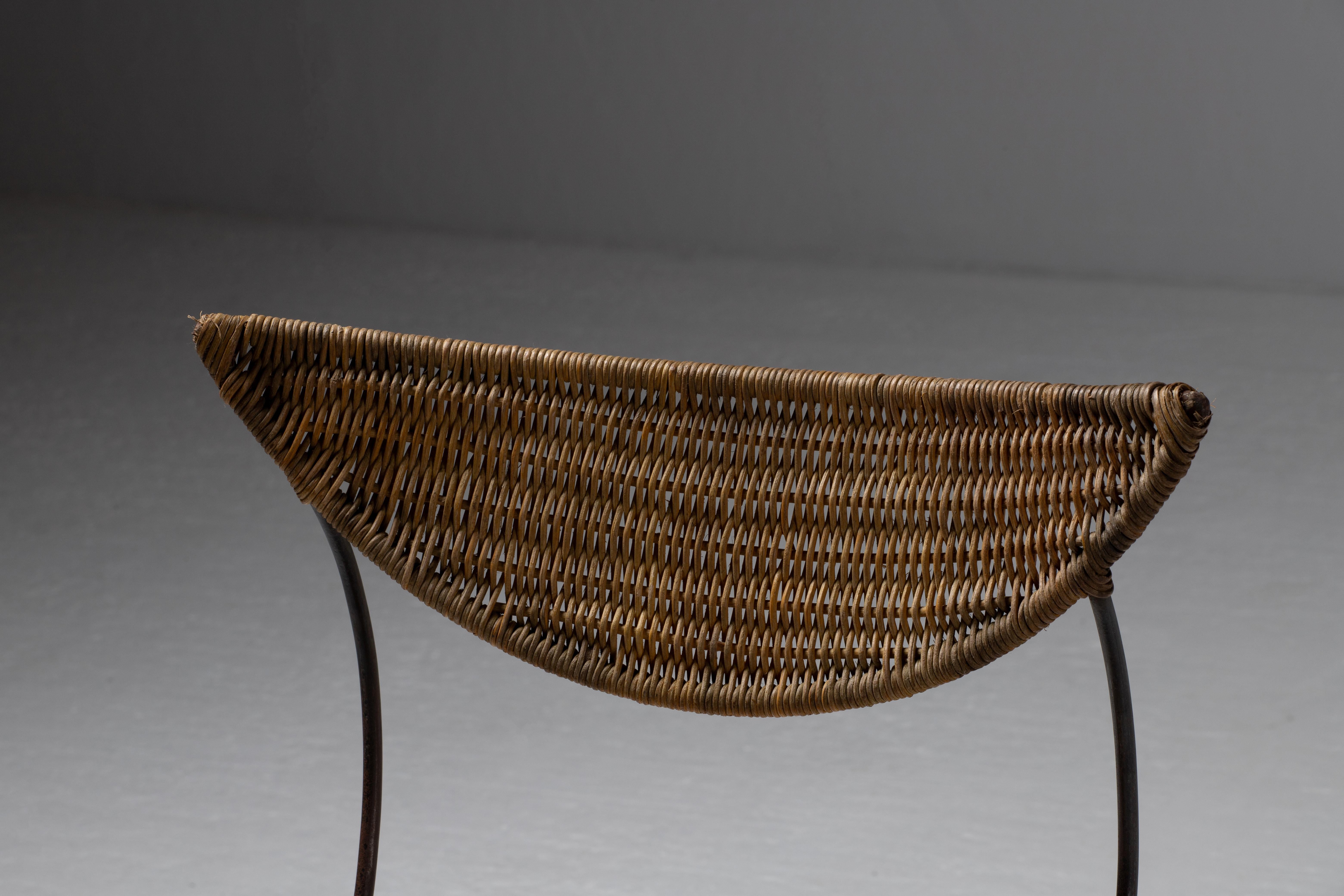 An arresting study of balance and tension, this sculptural chair defies the boundaries of conventional seating. With its woven rattan surface and sinuous iron frame, it evokes both organic fluidity and geometric precision, standing as an artifact of