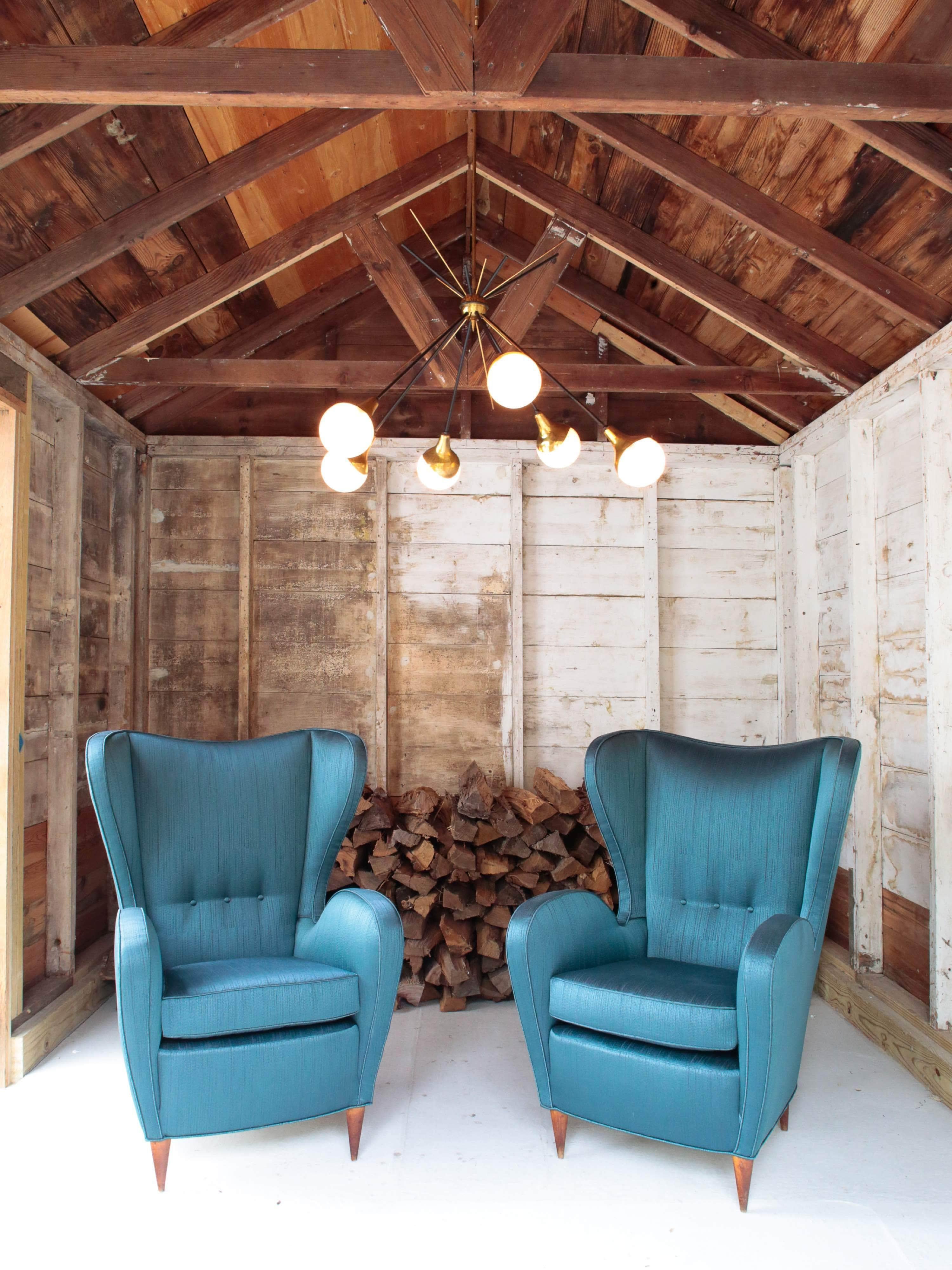 Stunning pair of Midcentury Italian wingback chairs re-upholstered in an Italian peacock blue silk stripe by Bergamo. It offers a high back and three tufted buttons that enhance the clean lines of this vintage frame and solid rosewood legs to