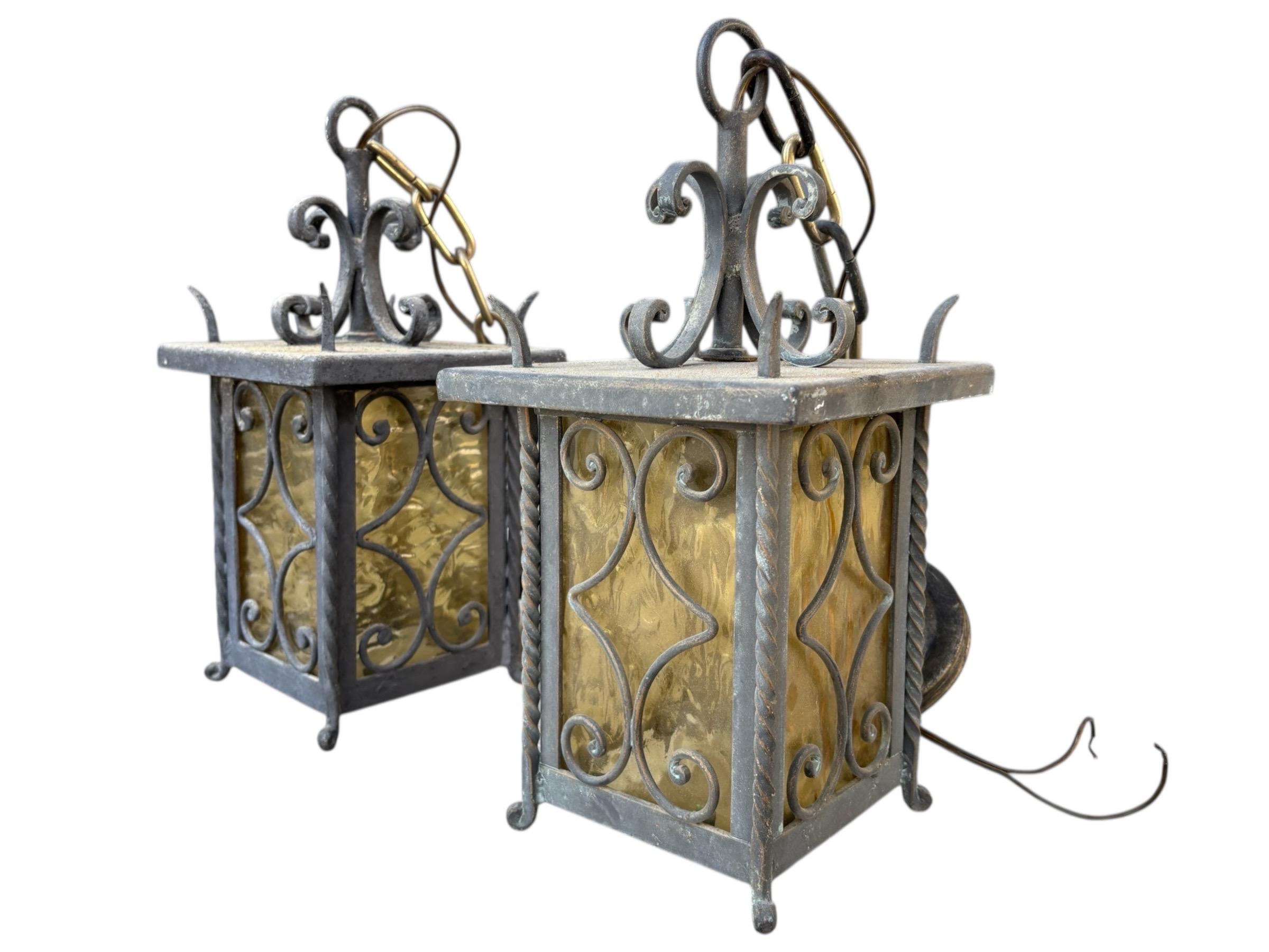 Coppia di lanterne da parete a sospensione italiane del 1950 circa. I pannelli in vetro ambrato sono fissati con montanti in ferro battuto a spirale e a torsione. È appeso con una catena in ottone e rifinito con una calotta in metallo dorato. La