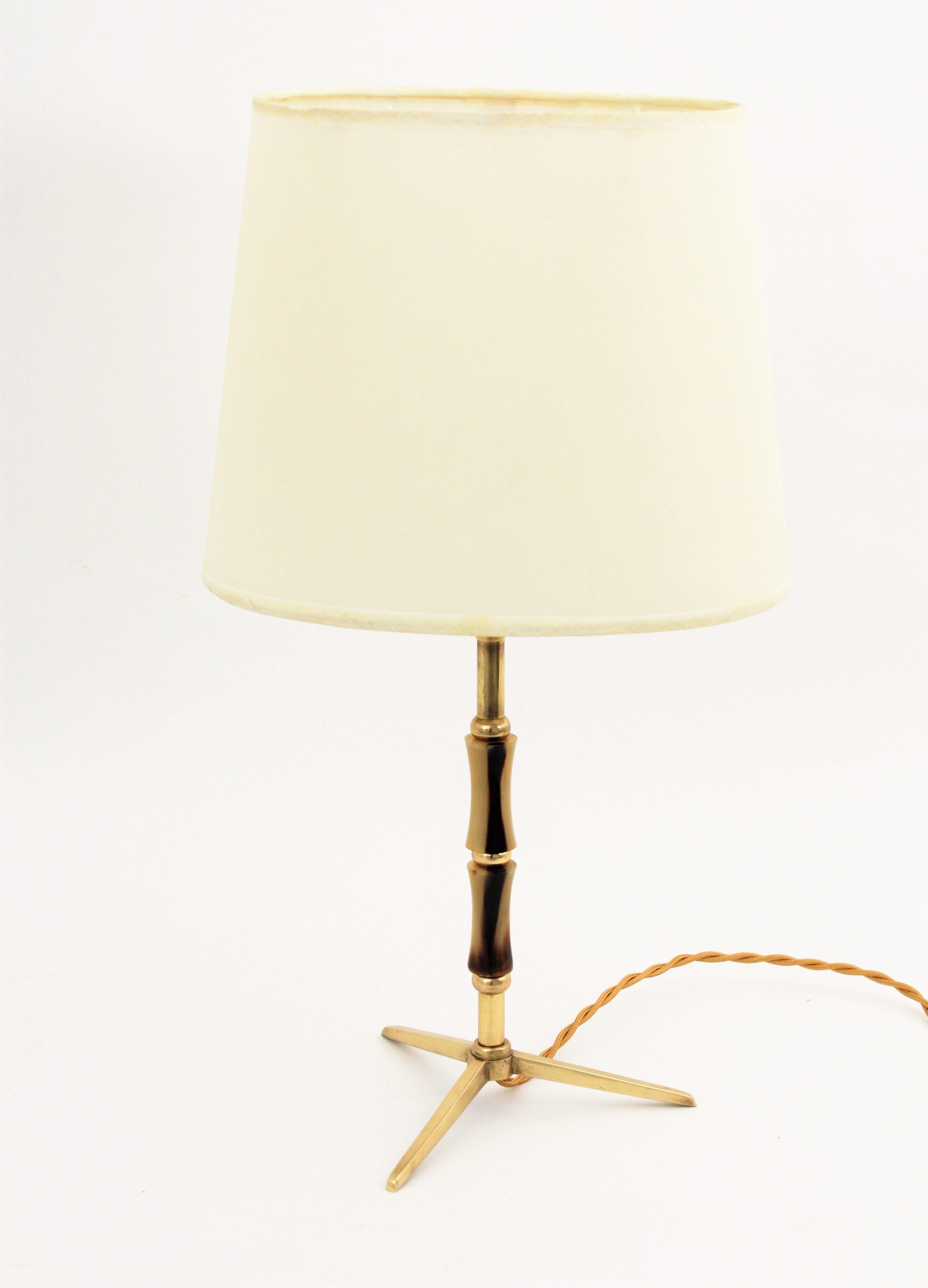 A brass tripod table lamp accented by acrylic details attributed to Jacques Adnet, France, 1950s.
This elegant table lamp is ornamented by faux bamboo details made of acrylic cylindrical pieces and brass rings. It wears its original shade that is in