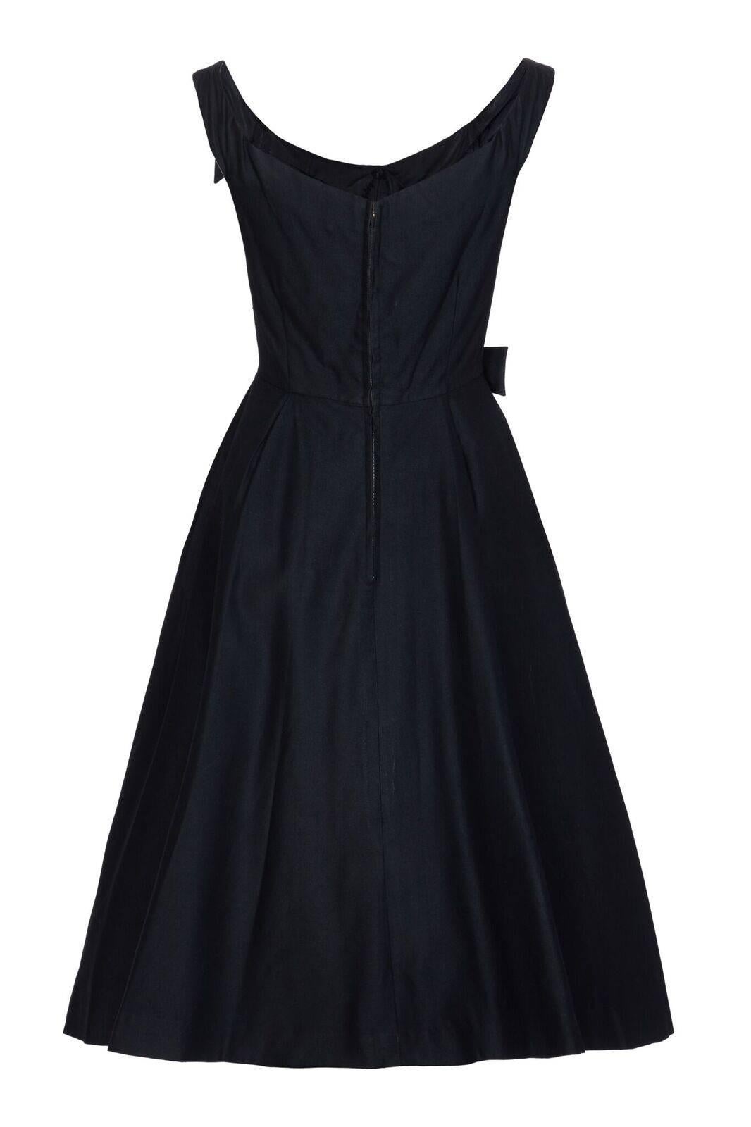 This striking 1950s New-Look style evening gown by Jacques Heim demonstrates some impeccable tailoring skills. The dress is of heavy starched black cotton and styled to flatter a classic hourglass silhouette. The wide angled straps graduate