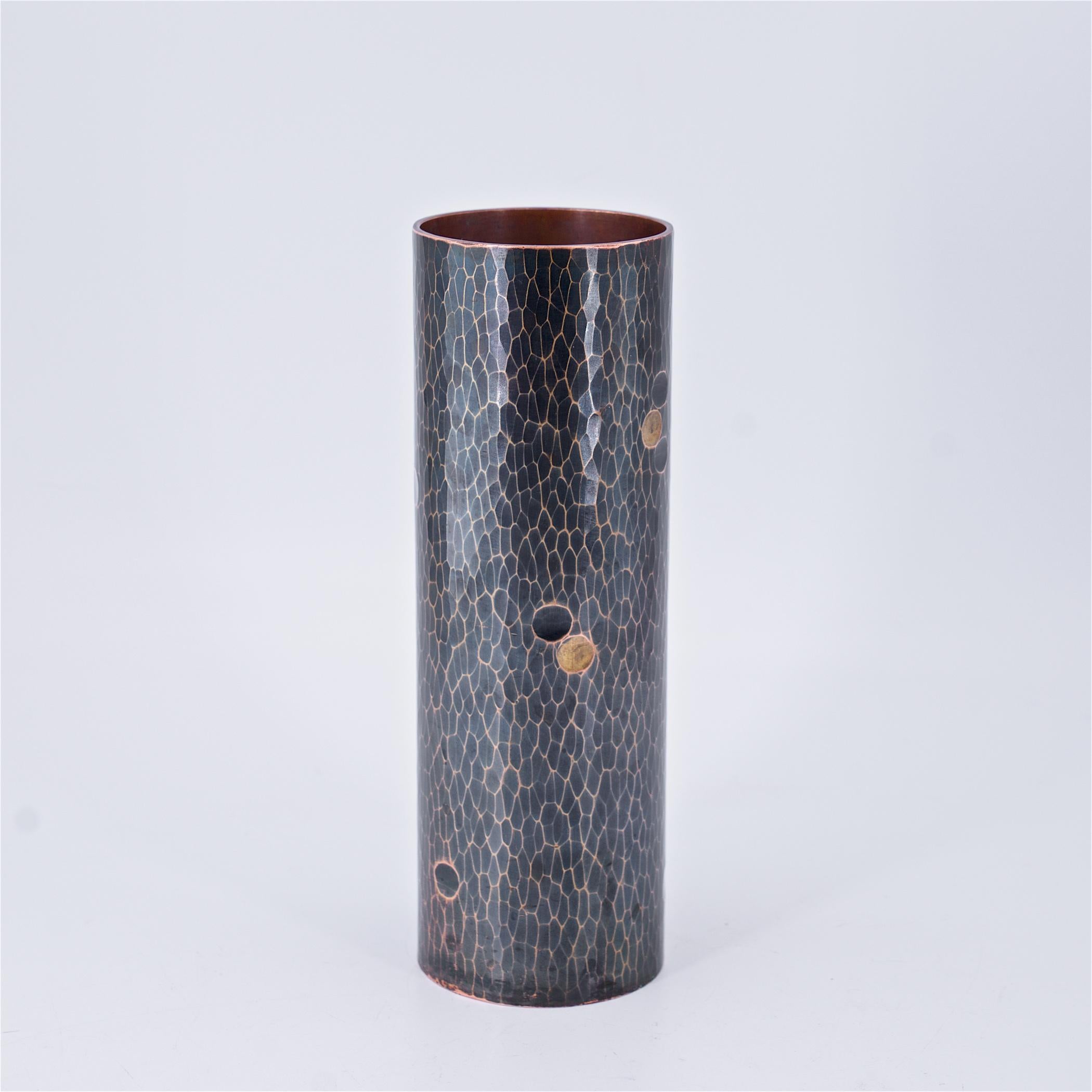A fine vintage mid-century Japanese bronze and brass cylinder vase with a Martelé finish. Black patinated surface, polished ridges, and brass inlaid dots. Impressed maker’s mark on verso; wealth, nobility, and logotype with symbols of water and