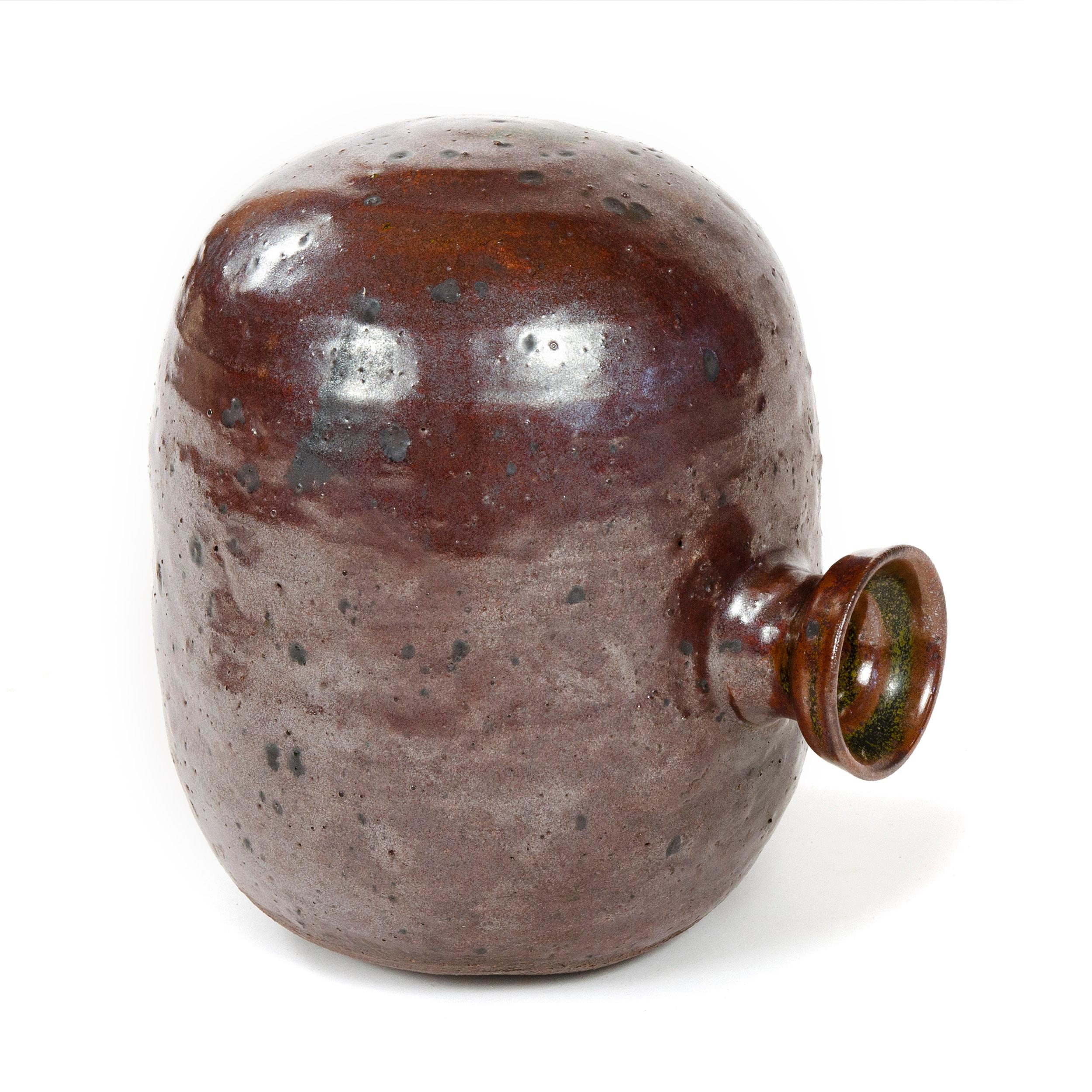 A brown glazed ceramic vessel with a center placed opening spout.