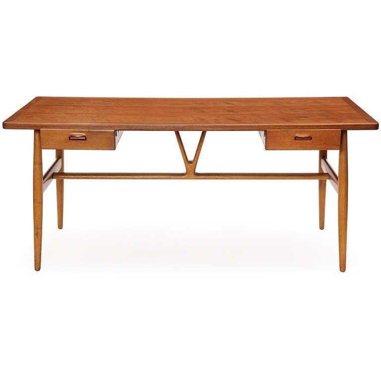 A refined and well proportioned writing desk having a teak top over twin floating drawers, resting on turned oak dowel legs braced by a carved central wishbone-shaped strut.