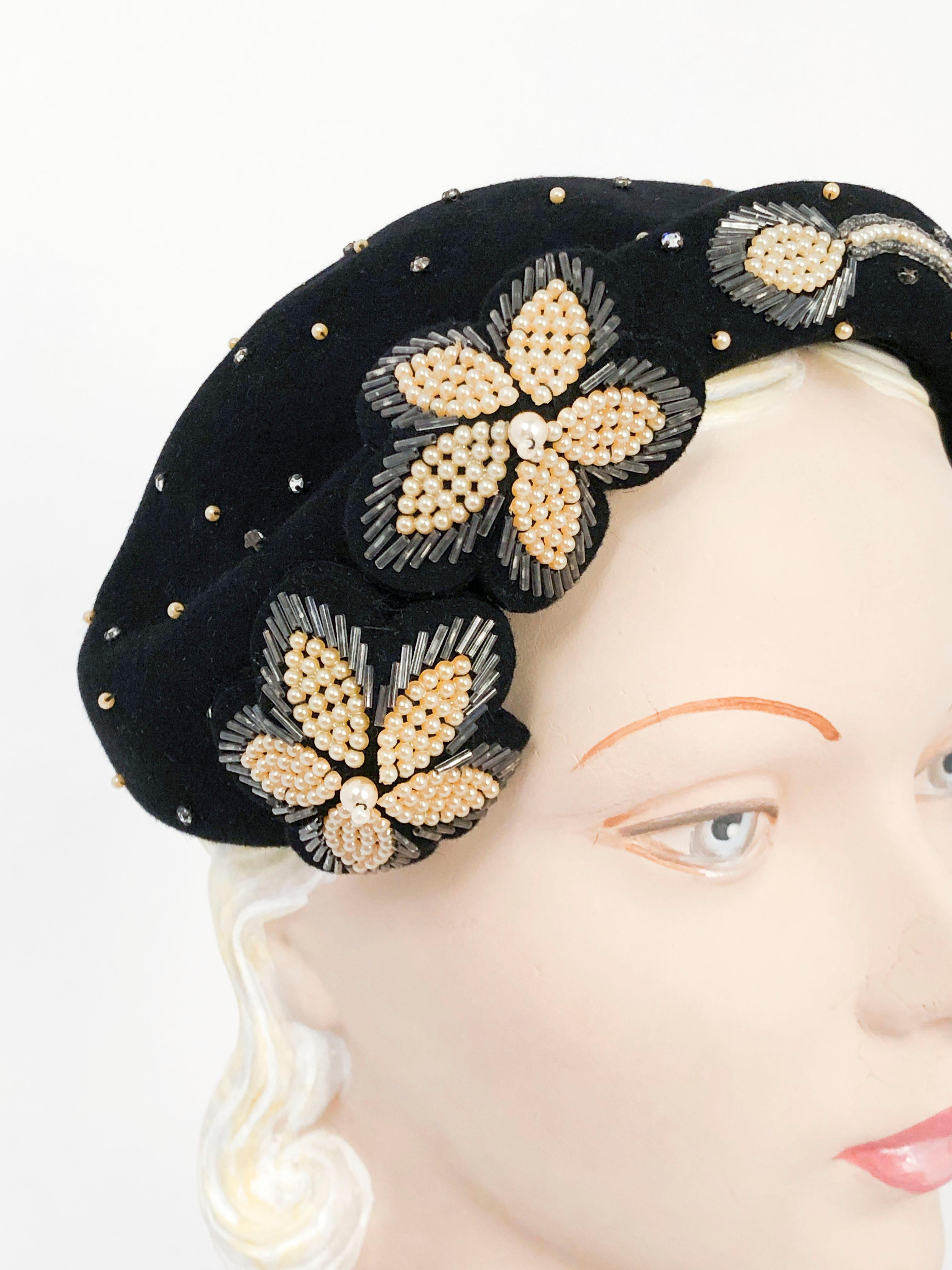1950s Black cashmere shaped hat featuring hand-beading, faux pearls, fastened rhinestones, and appliqué beaded flowers. The faux pearls and fastened rhinestones are place throughout the field of the hat