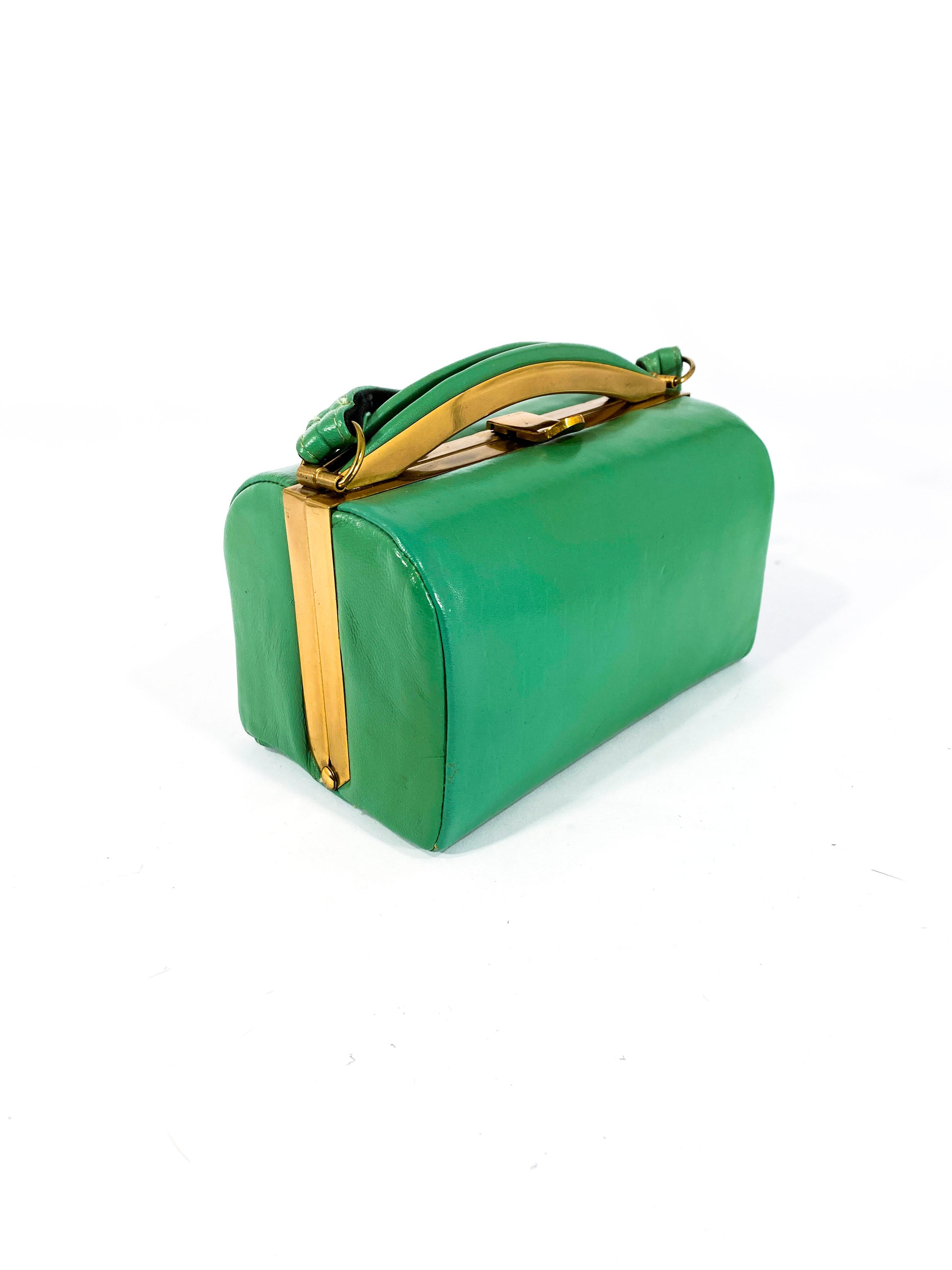 1950s Kelly green leatherette top handle bag with brass frame and hardware. The body of the bag is lined in black twill and has a centered metal zipper pocket. 