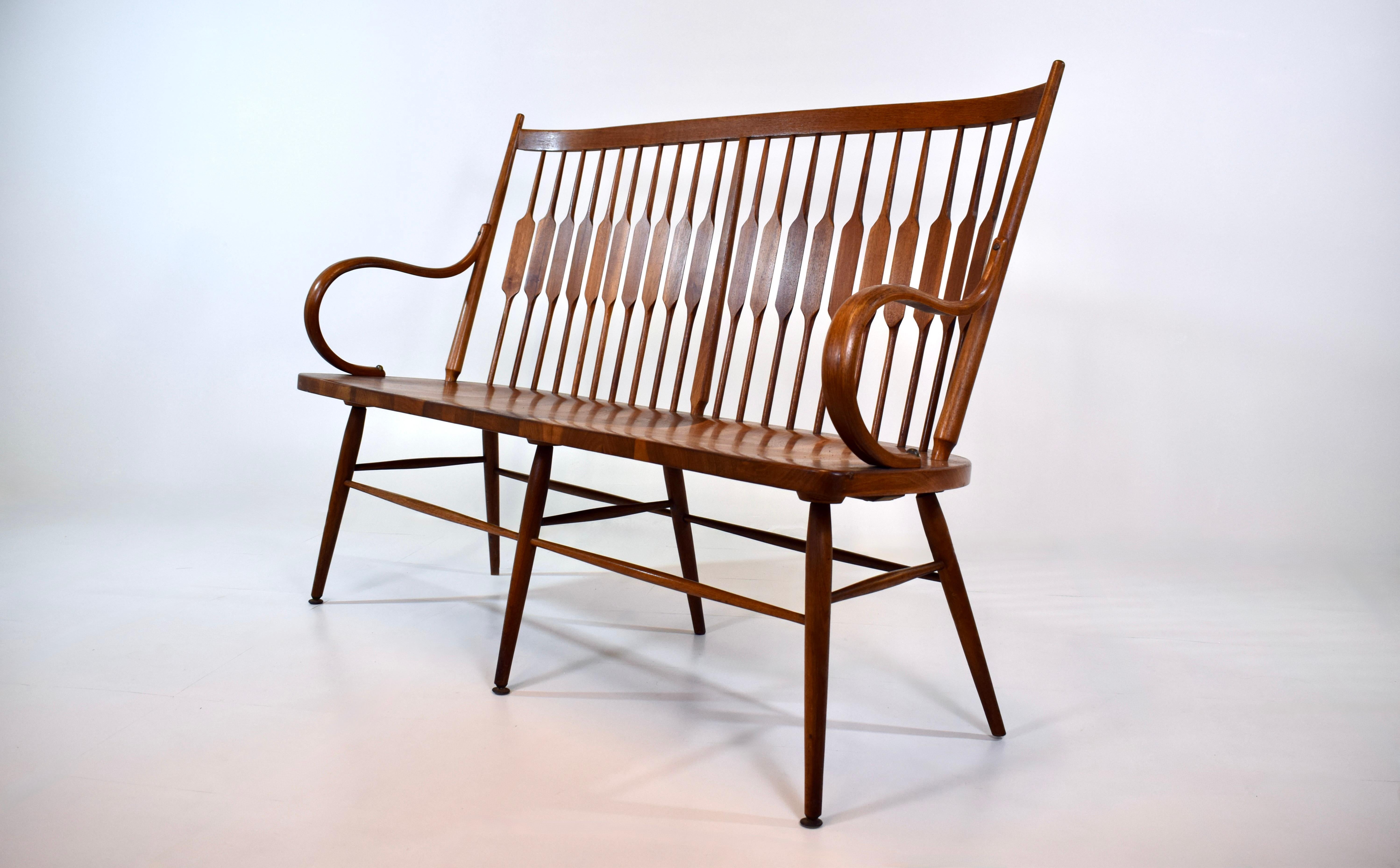 An exceptional mid 20th century spindle back bench designed by Kipp Stewart and Stewart MacDougall for Drexel Furniture. Constructed of solid walnut the bench features hand carved back splats with flattened form, stylish bentwood arms with brass