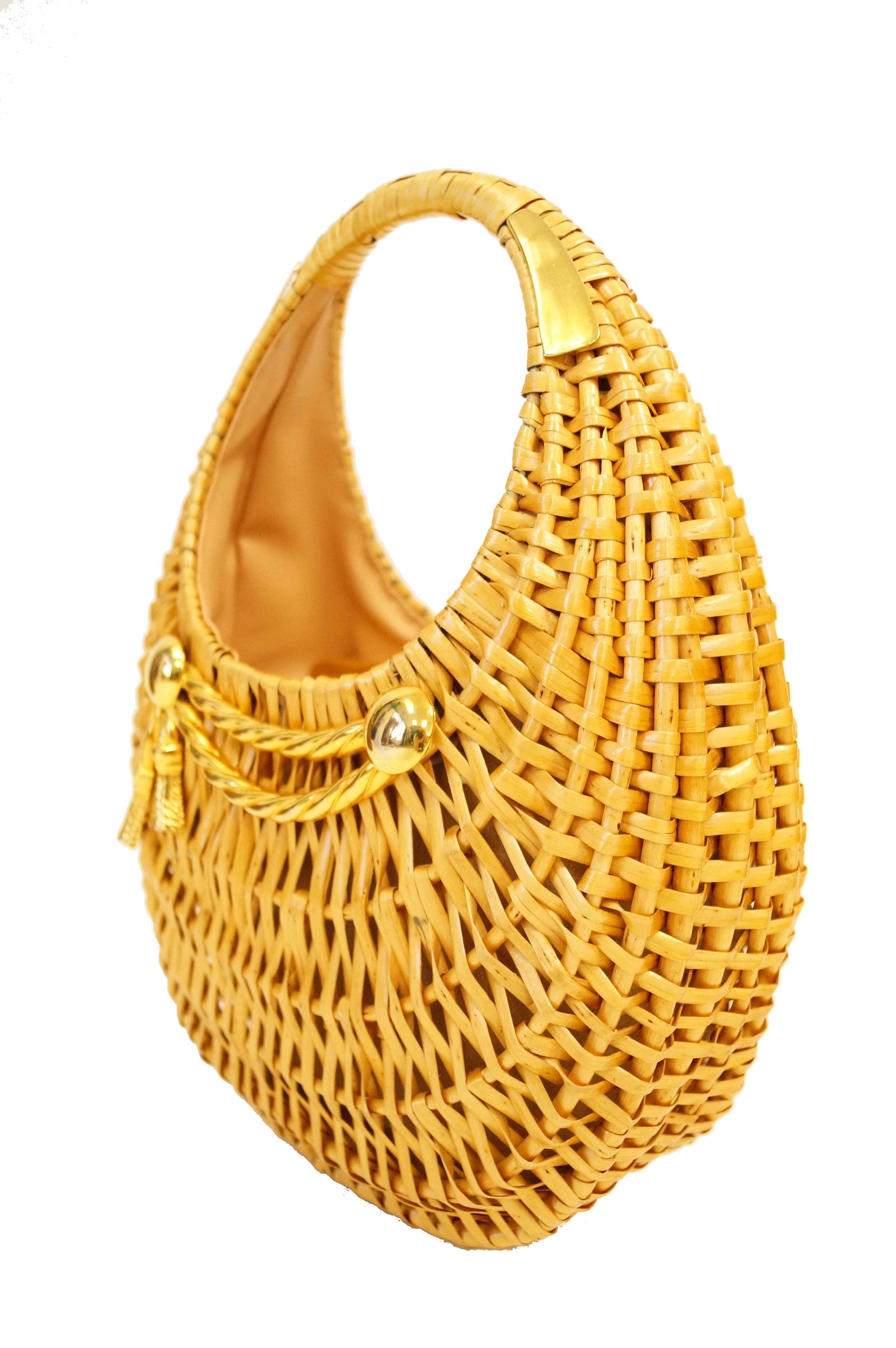 Beautifully woven flat reed handbag in a crescent shape by Koret! The handbag is oval, features a gold tone tassel motif, and a large round handle accented by gold clips. The interior is lined in tan faux leather, and features a snap pocket. Perfect