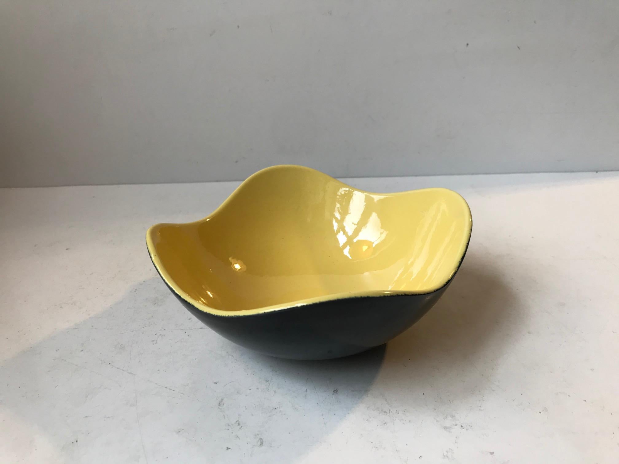 A wavy asymmetrical ceramic bowl or dish executed in black and yellow glazes. It is called Congo and was designed and manufactured by Kronjyden Randers, circa 1950-59. It measures 17 cm in diameter and has a height of 7 cm.