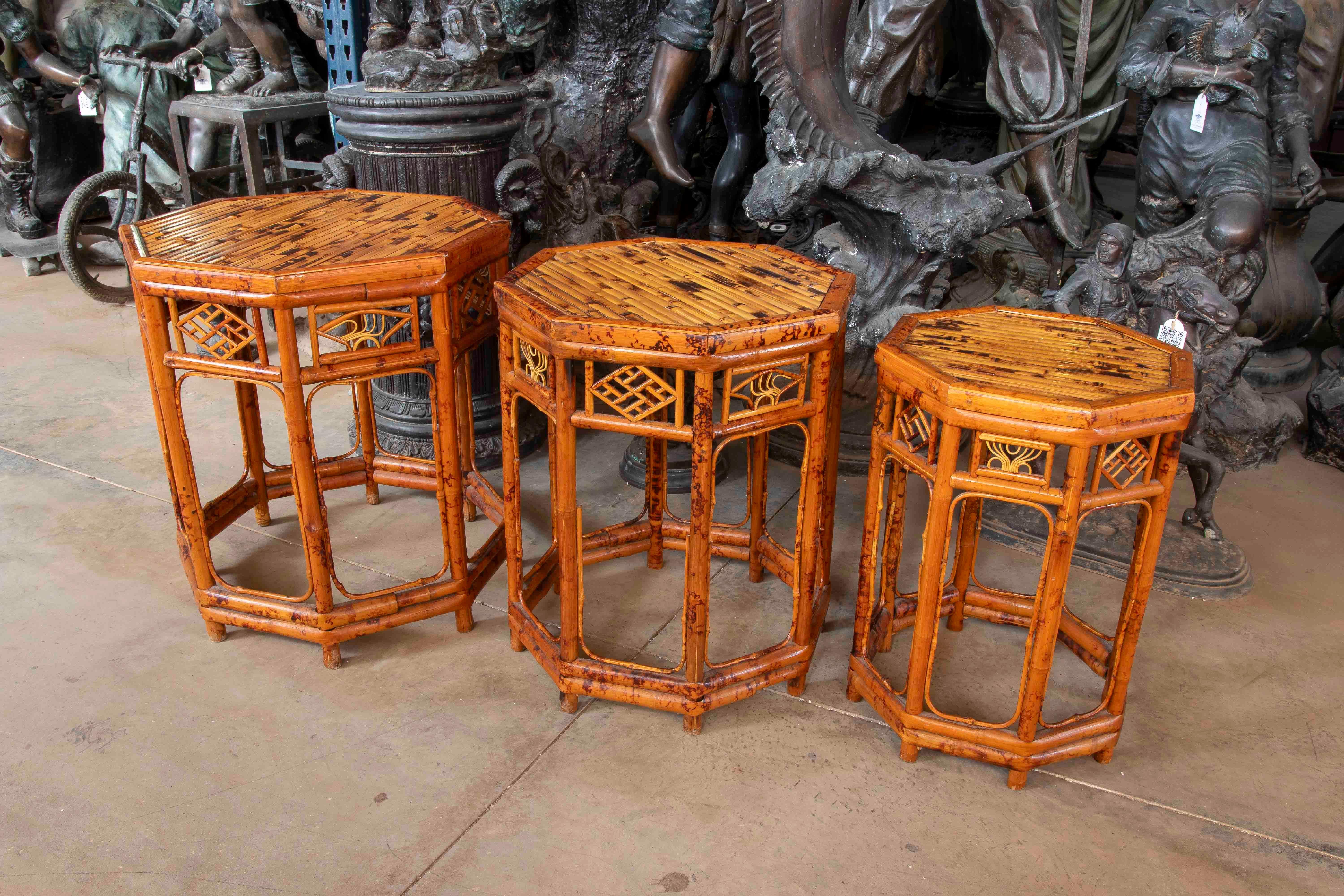 Un elegante set di tre tavolini di ispirazione orientale, realizzati in bambù naturale con finitura laccata color miele. Ogni tavolo presenta una struttura ottagonale con dettagli traforati sui lati che evocano motivi tradizionali cinesi, come il