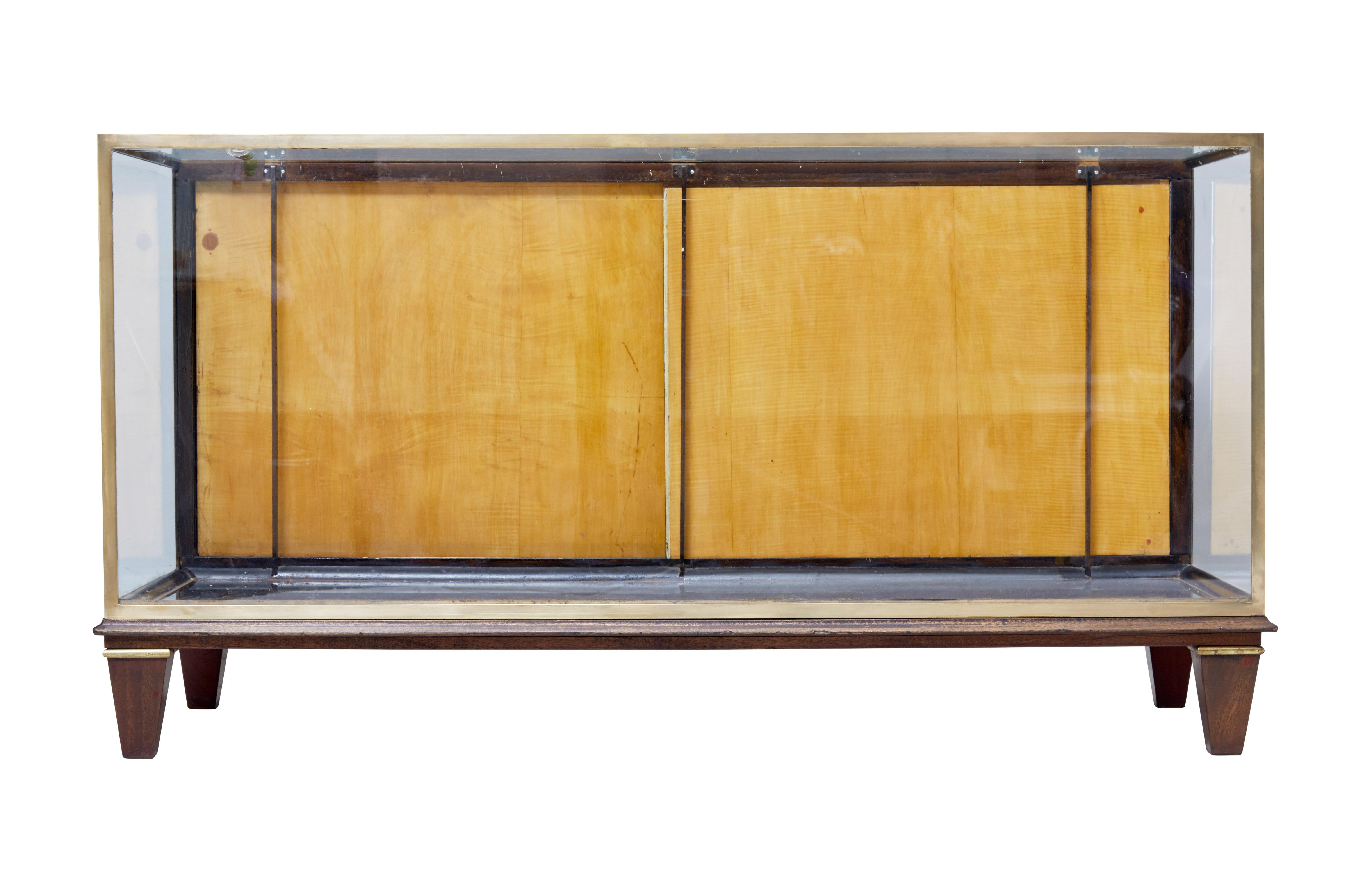 Large floor standing shop display, circa 1950.

Thick brass frame out edge, glazed front, sides and top. Teak sliding doors to the reverse.

Ideal for a shop display and having a shelf fitted inside.

Standing on brass and teak tapering